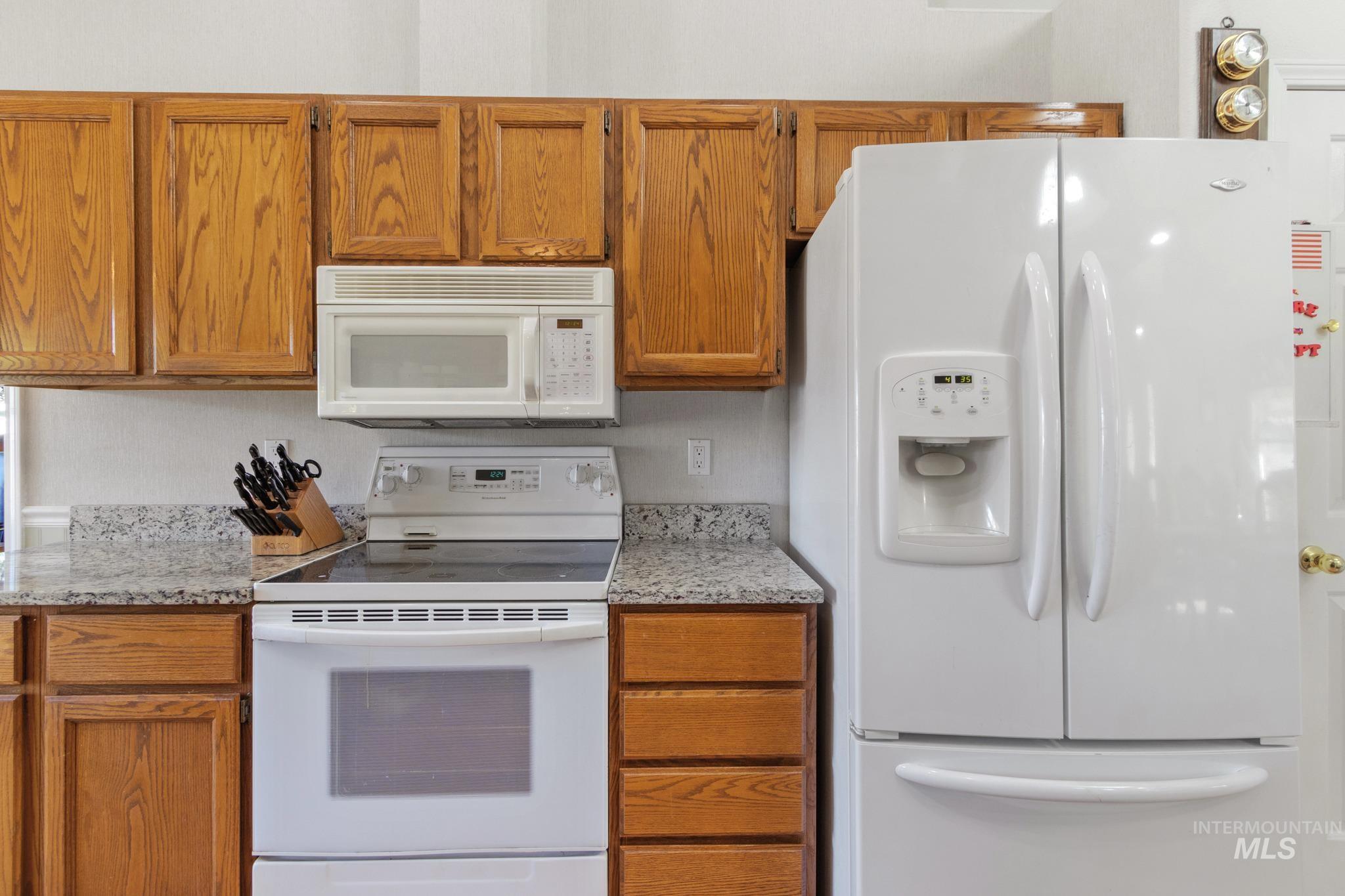 Kitchen with white appliances, brown cabinets, and light stone counters