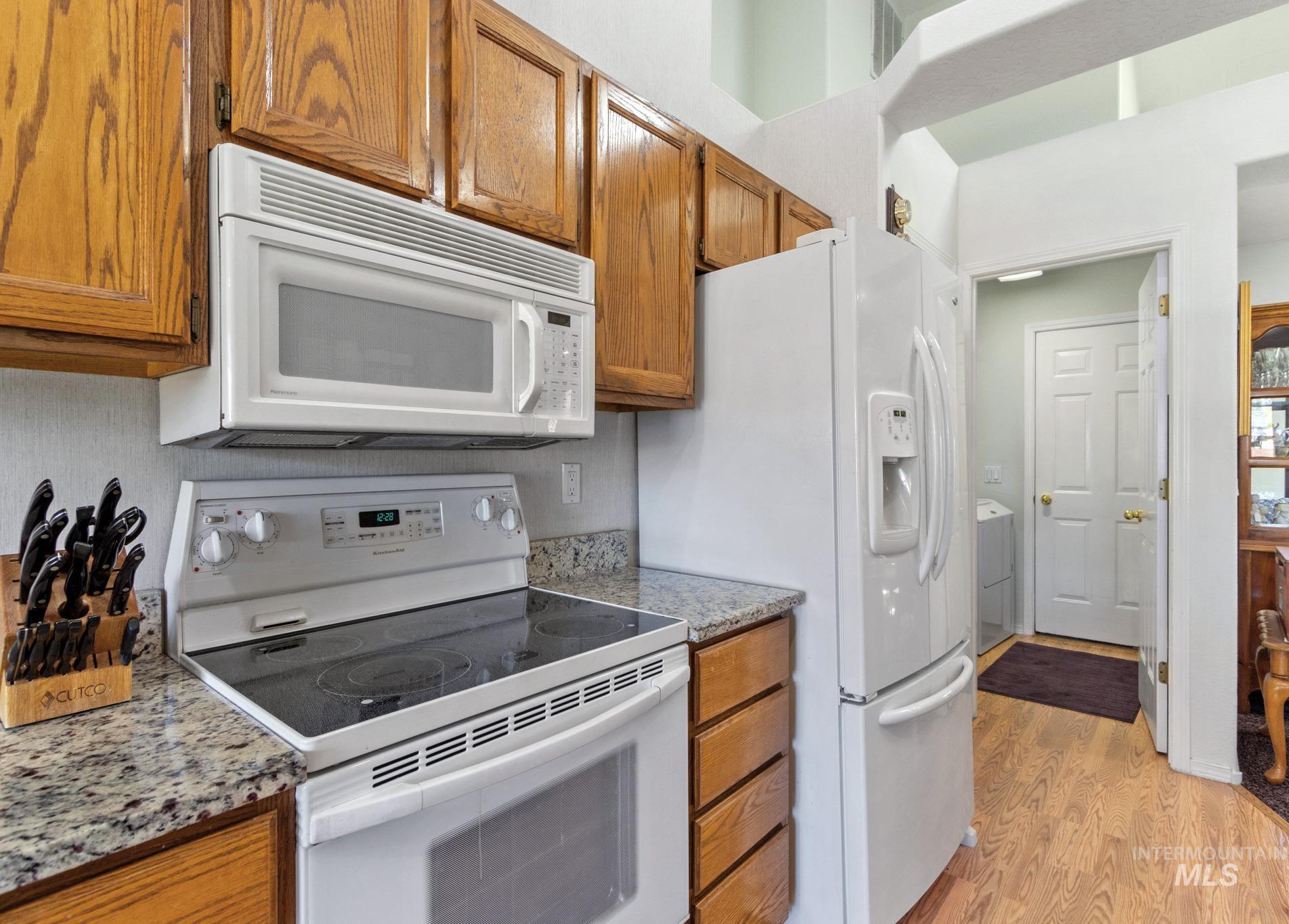 Kitchen featuring white appliances, brown cabinetry, light wood-style flooring, and light stone counters