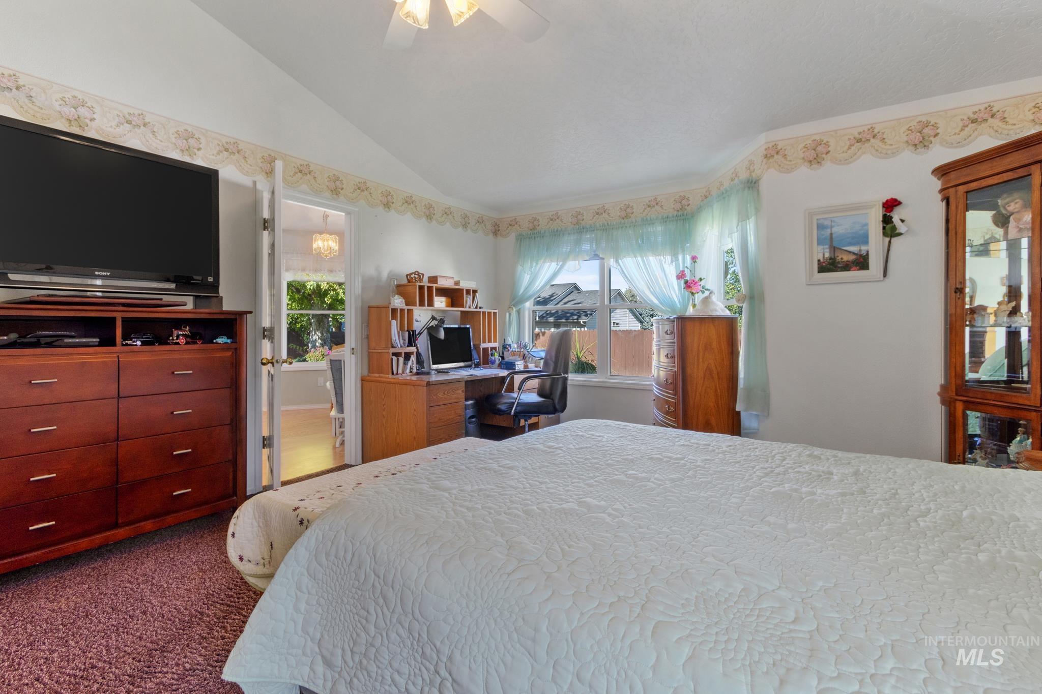Bedroom with vaulted ceiling, an office area, ceiling fan, and dark carpet