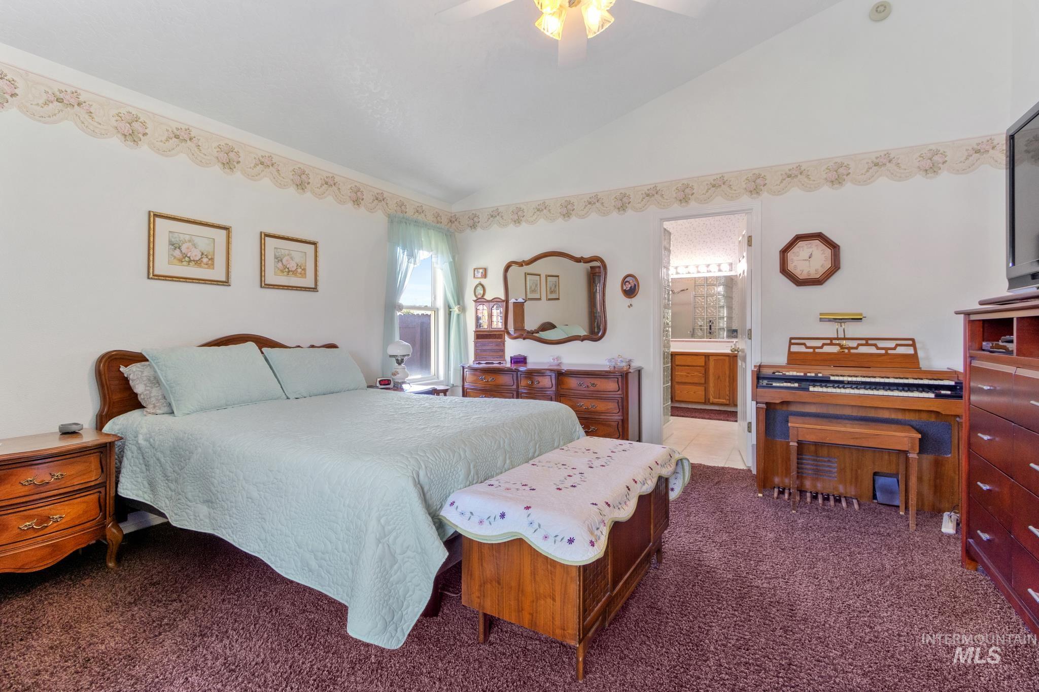 Bedroom with vaulted ceiling, dark carpet, a ceiling fan, and ensuite bath