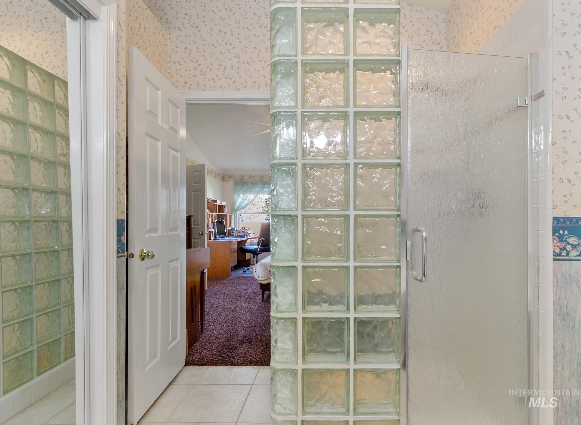 Ensuite bathroom featuring wallpapered walls, a stall shower, light tile patterned floors, and light carpet