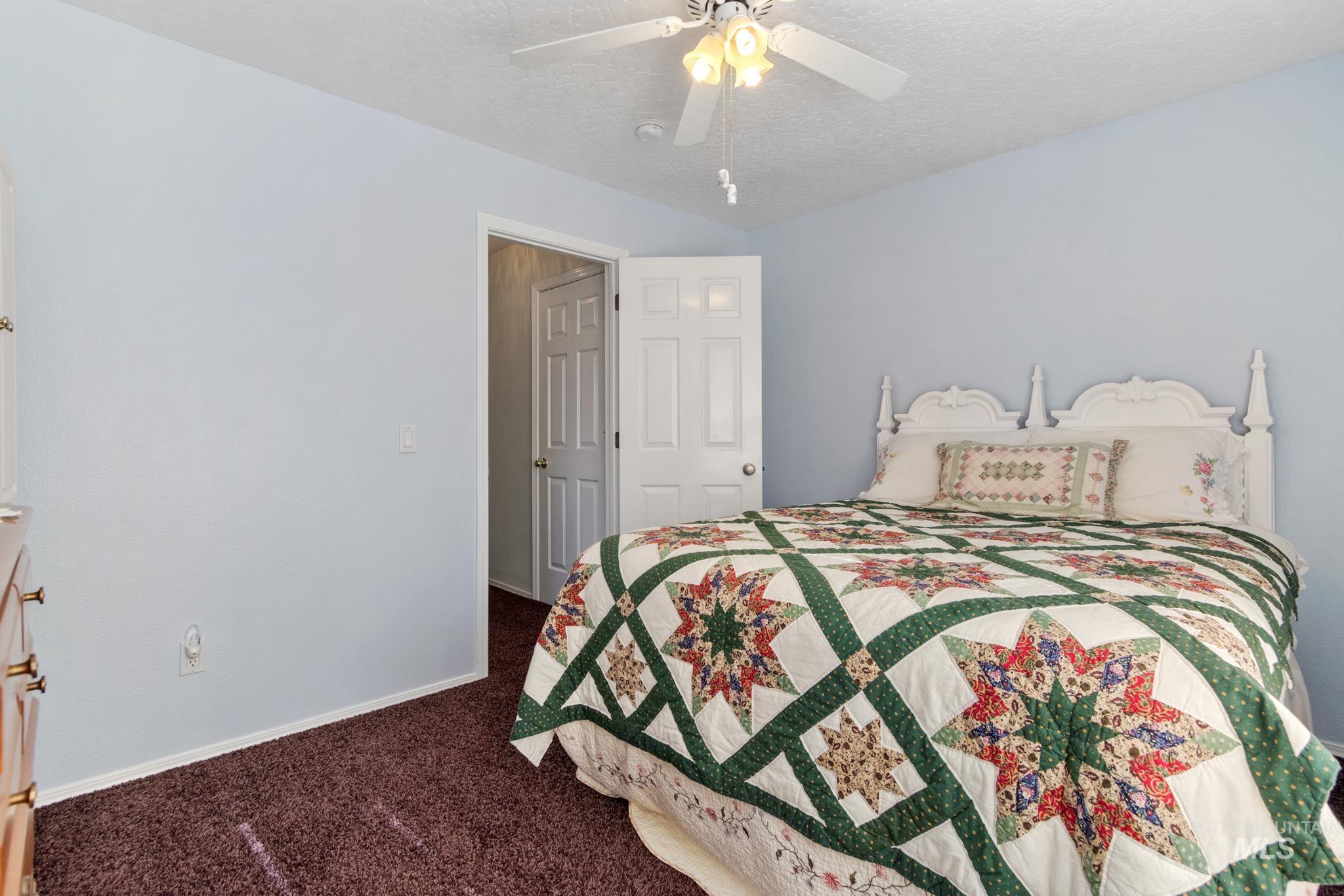 Bedroom with dark colored carpet, a ceiling fan, and a textured ceiling
