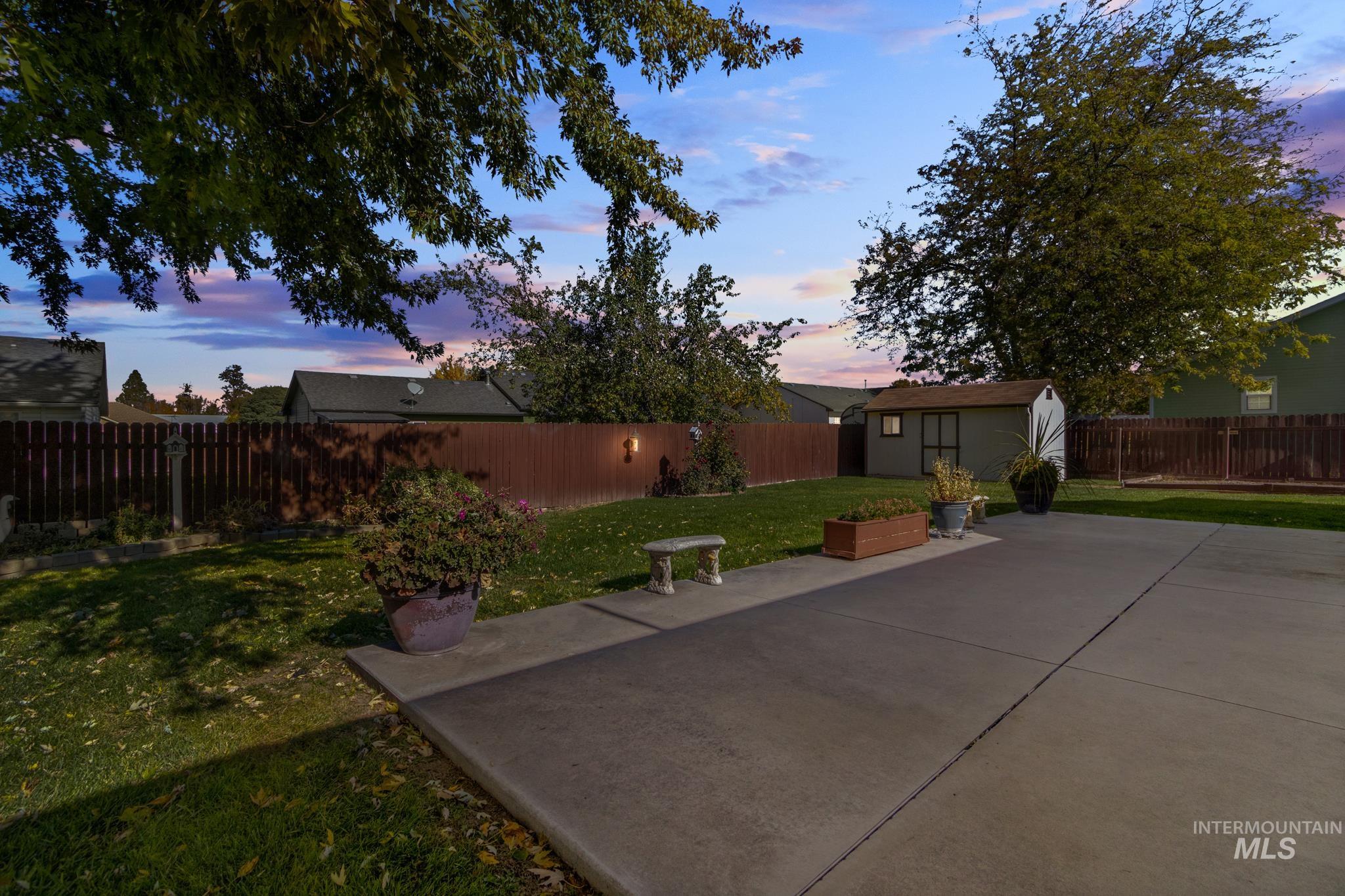 Yard at dusk featuring a shed, a fenced backyard, and a patio area