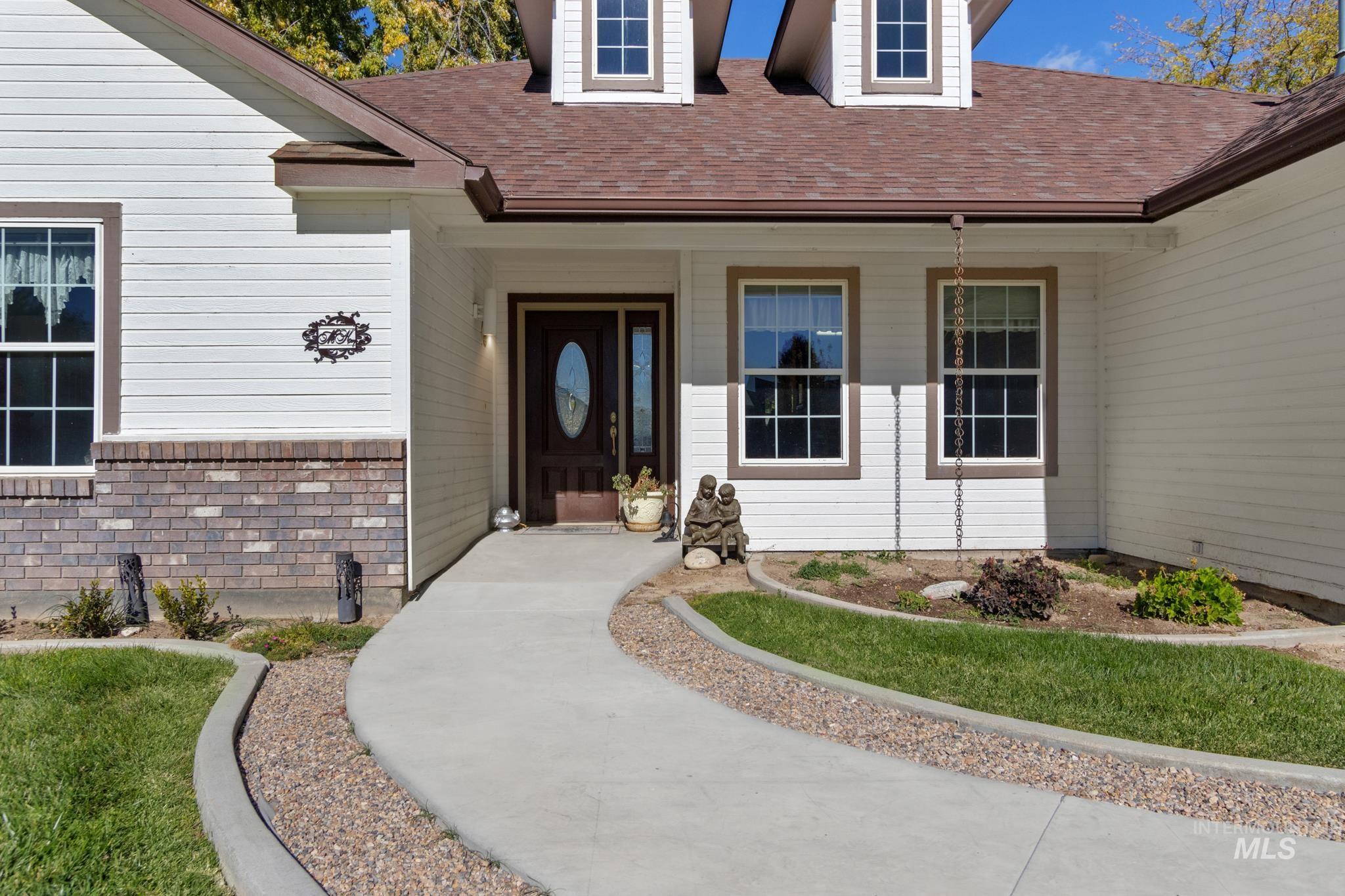Entrance to property featuring roof with shingles, covered porch, and brick siding