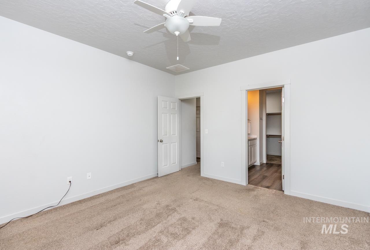 Unfurnished bedroom with carpet, ensuite bathroom, a textured ceiling, and a ceiling fan