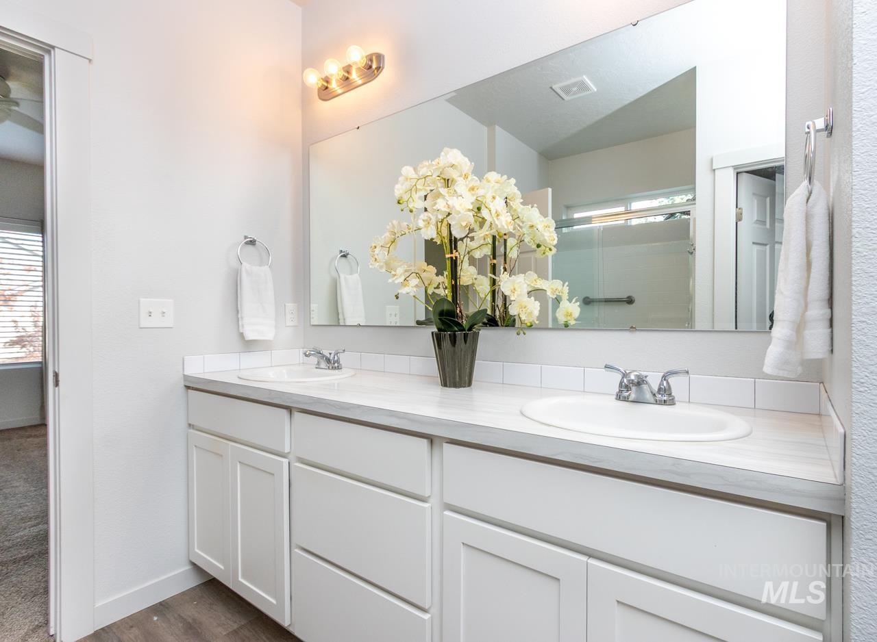 Bathroom with double vanity, a shower with door, and dark wood-type flooring