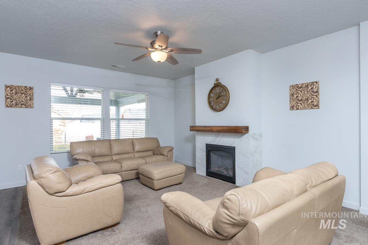 Living area with ceiling fan, a tiled fireplace, a textured ceiling, and carpet