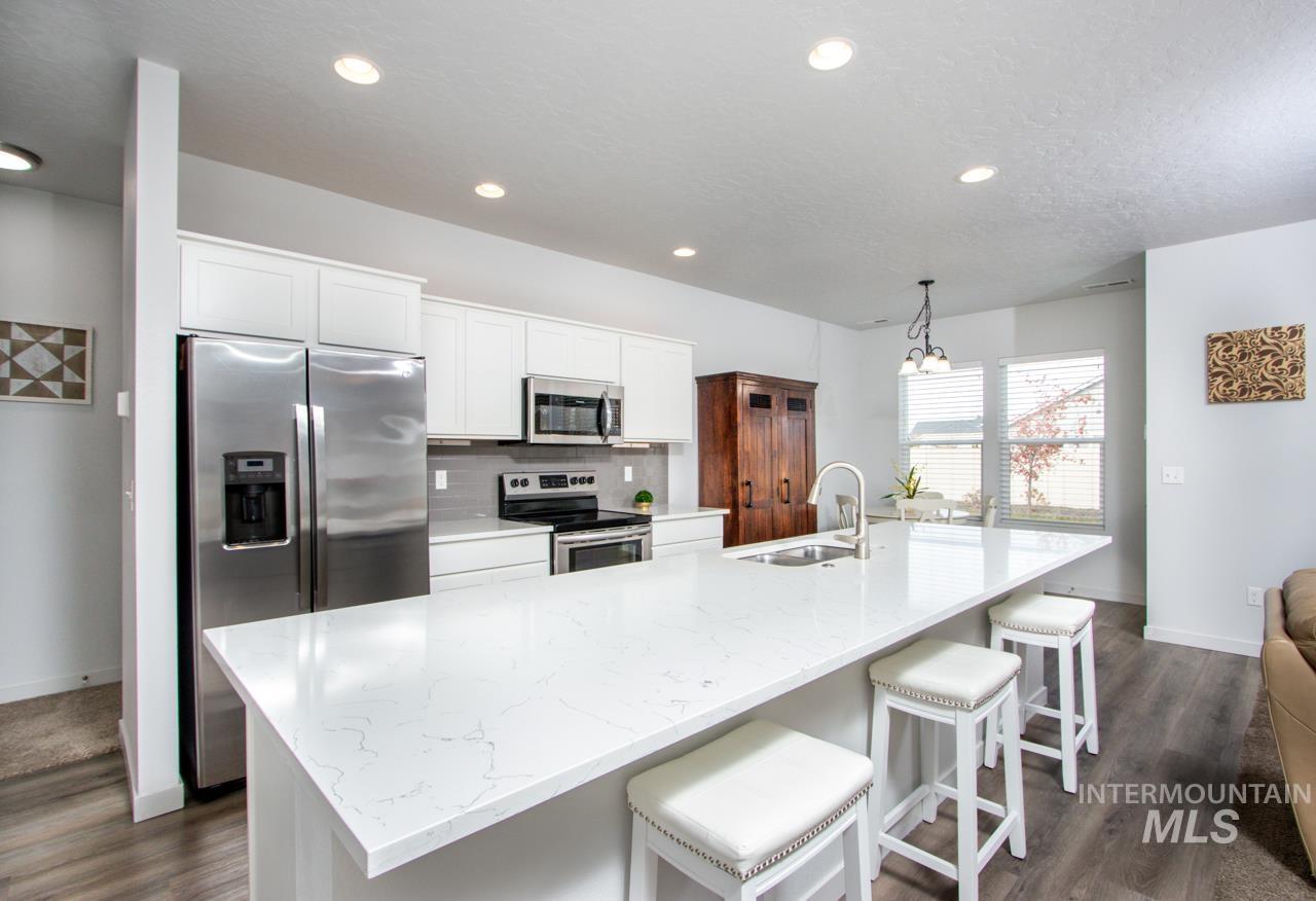 Kitchen with tasteful backsplash, white cabinets, stainless steel appliances, light stone countertops, and a spacious island