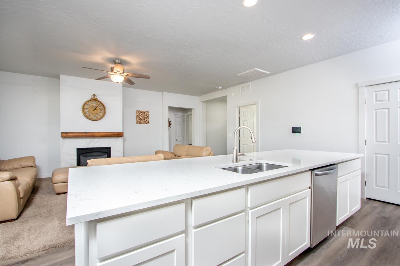 Kitchen featuring open floor plan, white cabinetry, a textured ceiling, light stone counters, and dishwasher