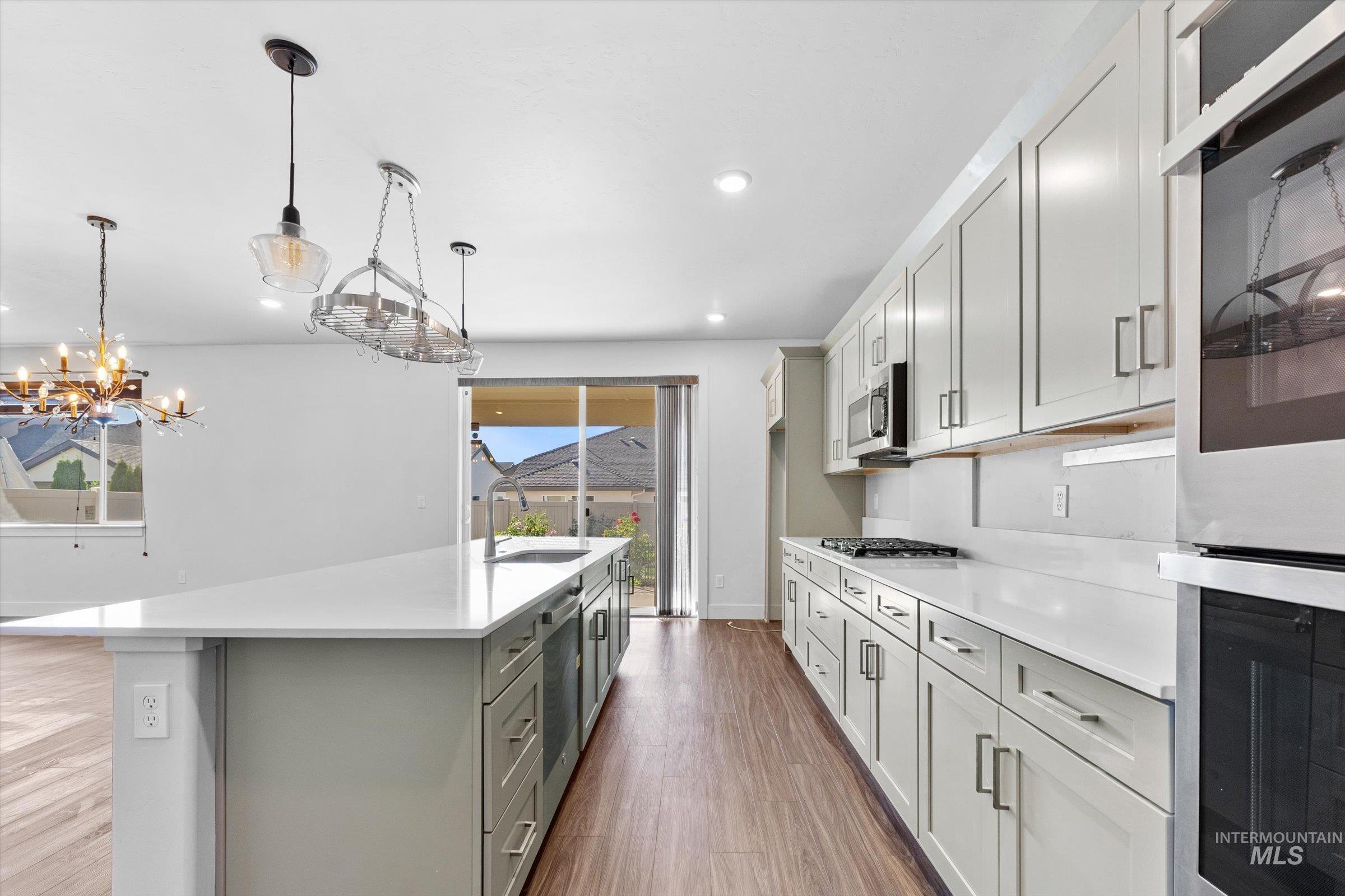 Kitchen featuring stainless steel appliances, dark wood finished floors, an island with sink, pendant lighting, and light stone countertops