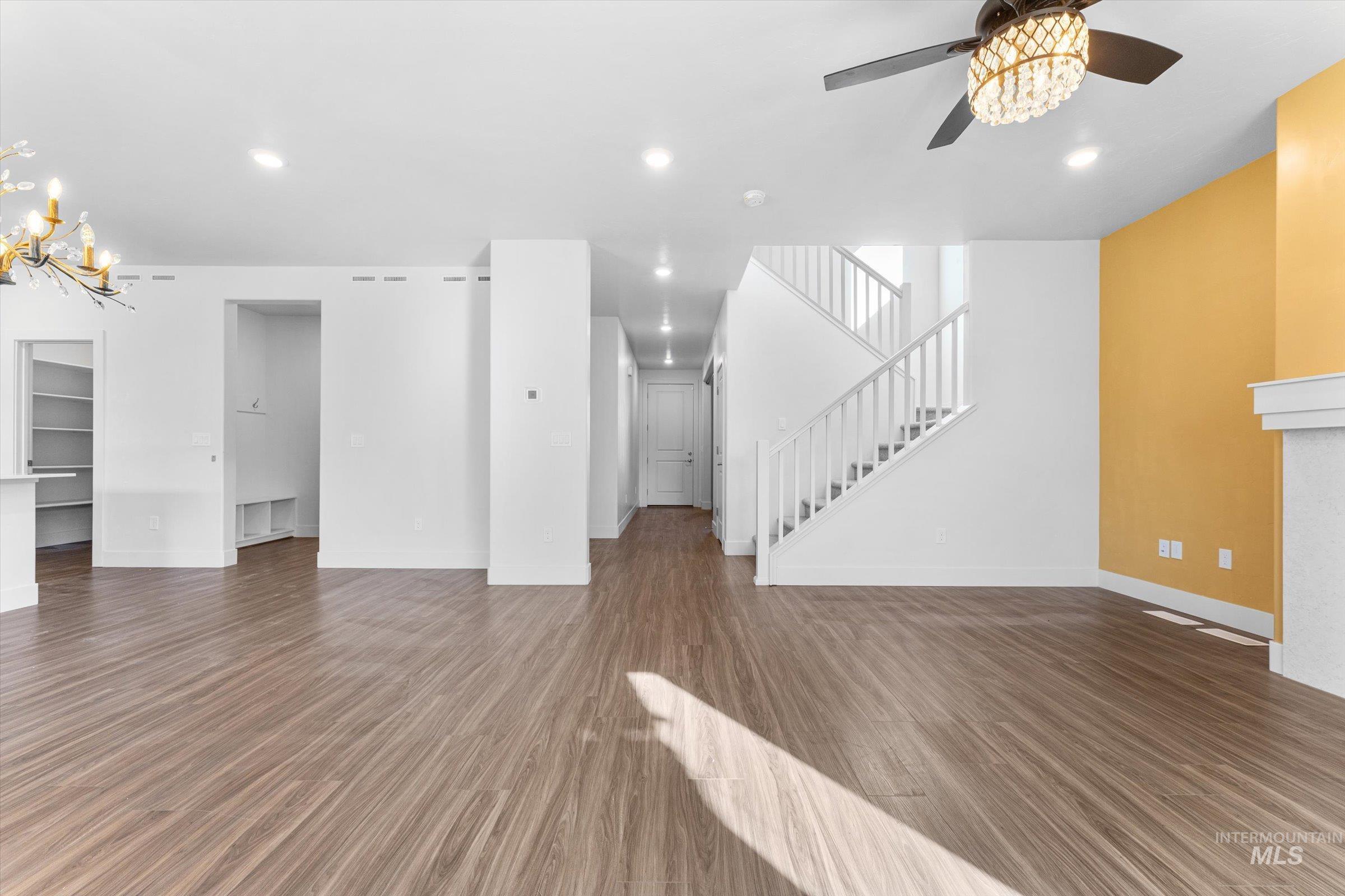 Unfurnished living room featuring dark wood-style floors, a chandelier, recessed lighting, stairs, and a ceiling fan