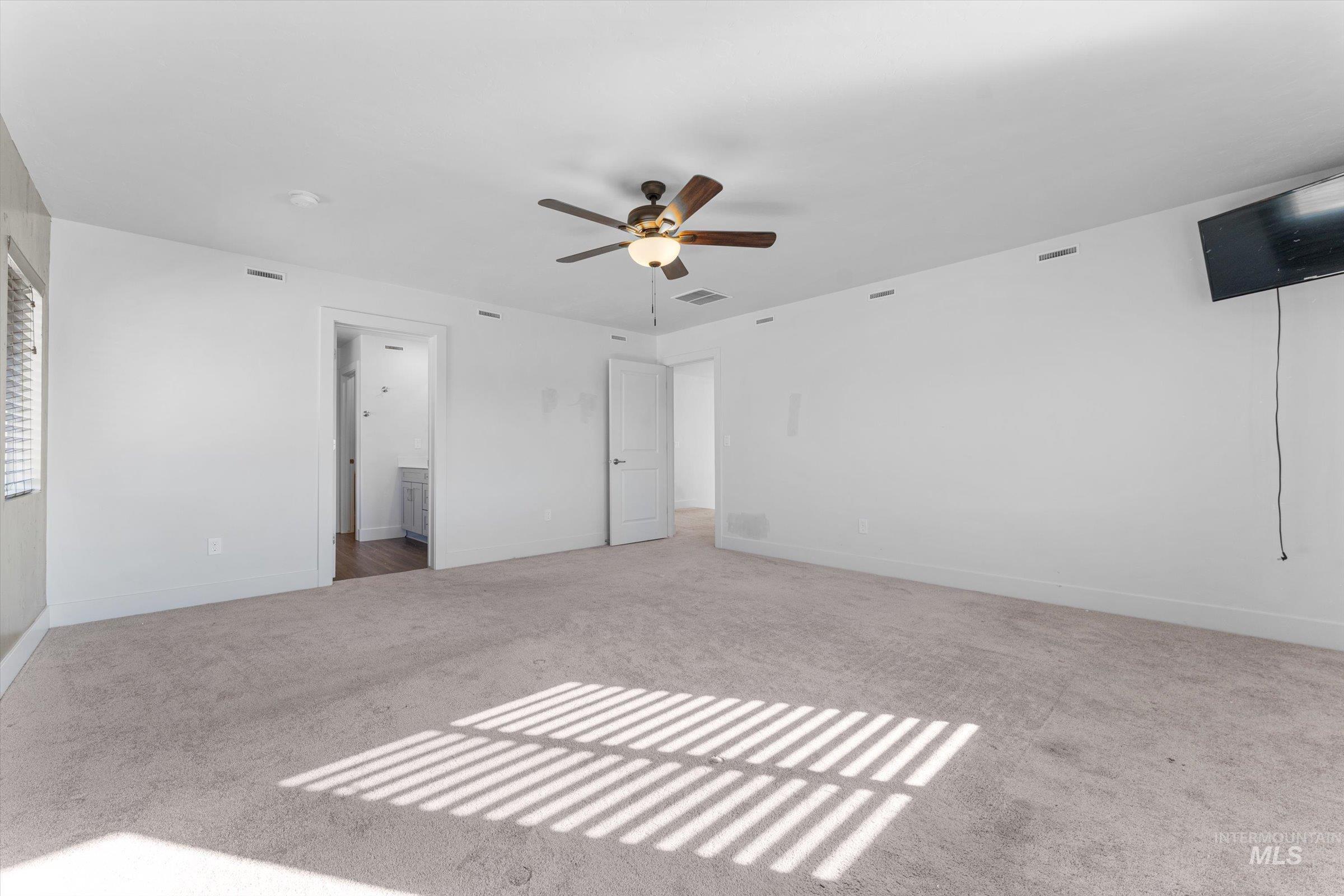 Unfurnished bedroom featuring light colored carpet, ceiling fan, and ensuite bathroom