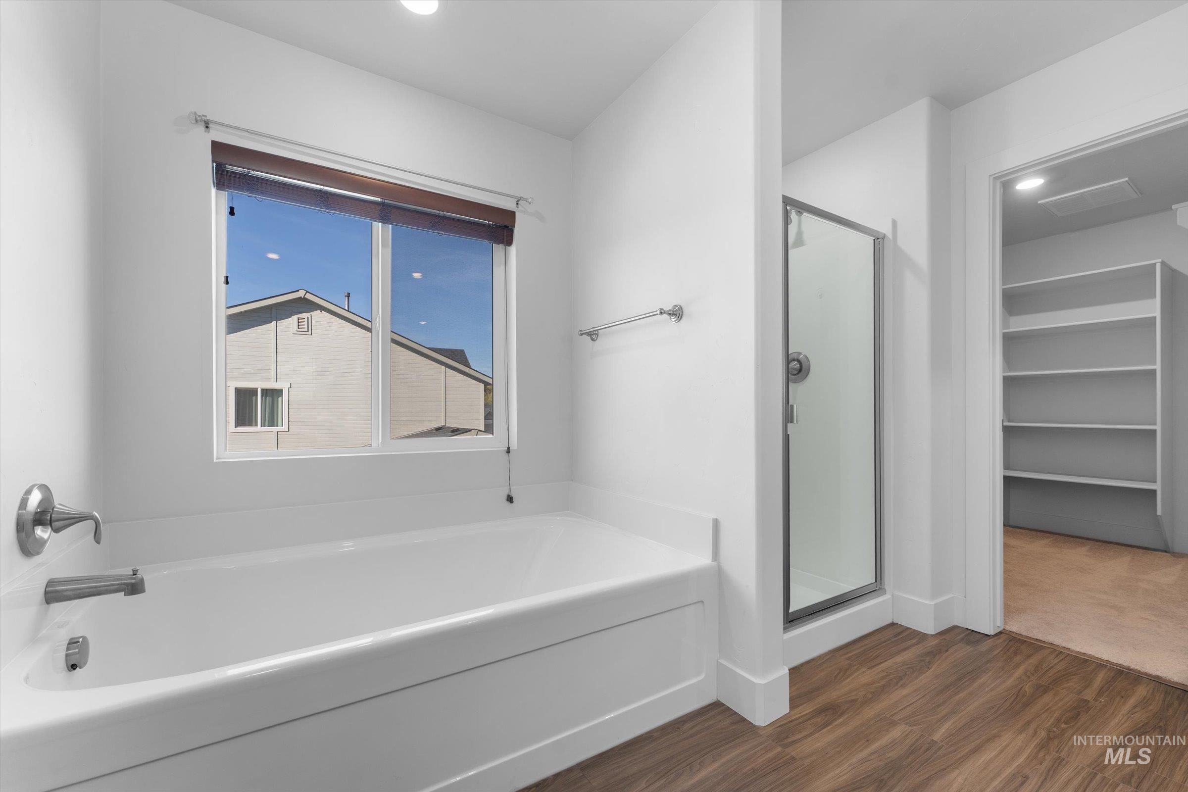 Full bathroom featuring a garden tub, a spacious closet, dark wood-type flooring, and a stall shower