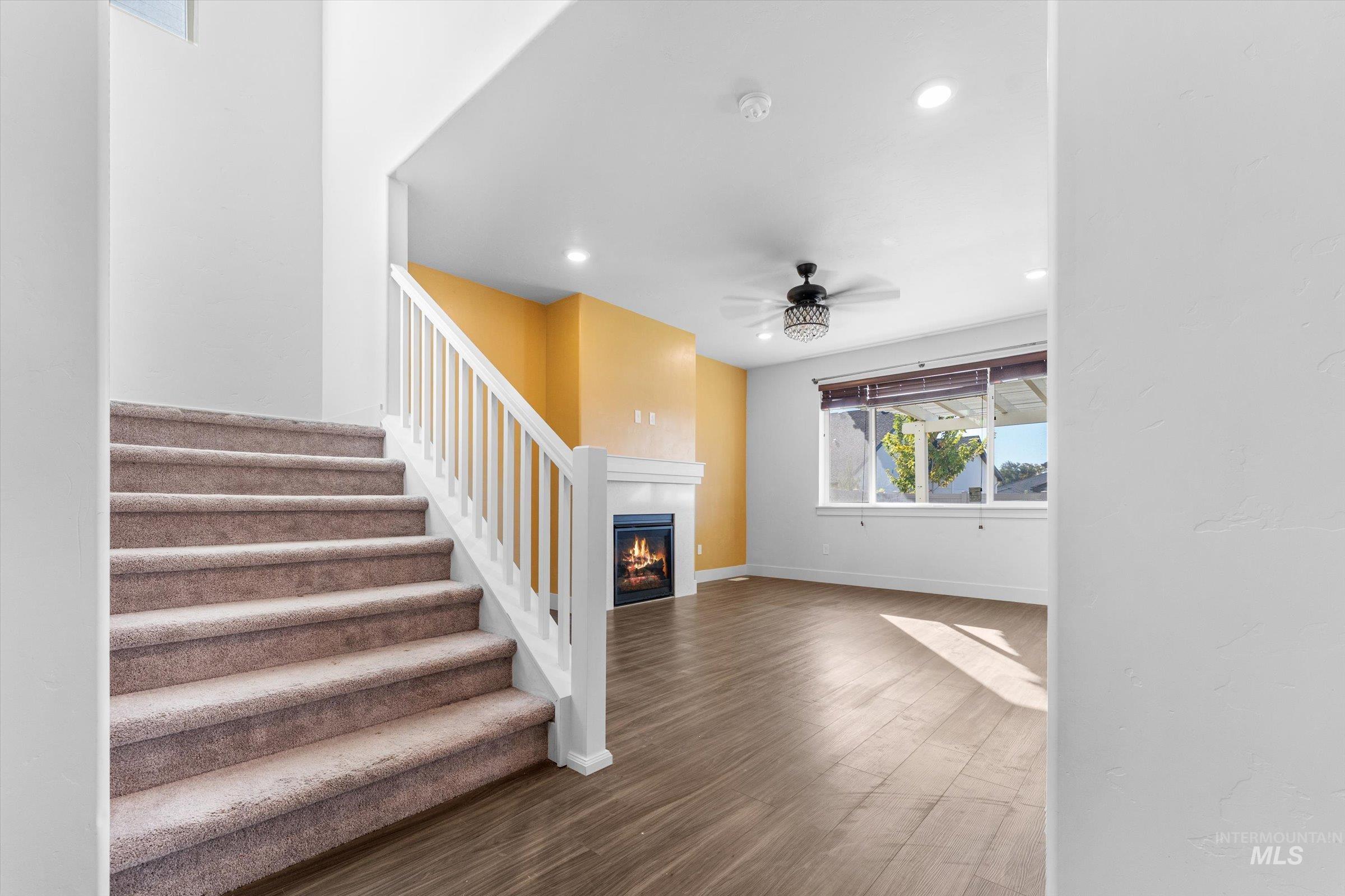 Stairs with wood finished floors, recessed lighting, a lit fireplace, and a ceiling fan