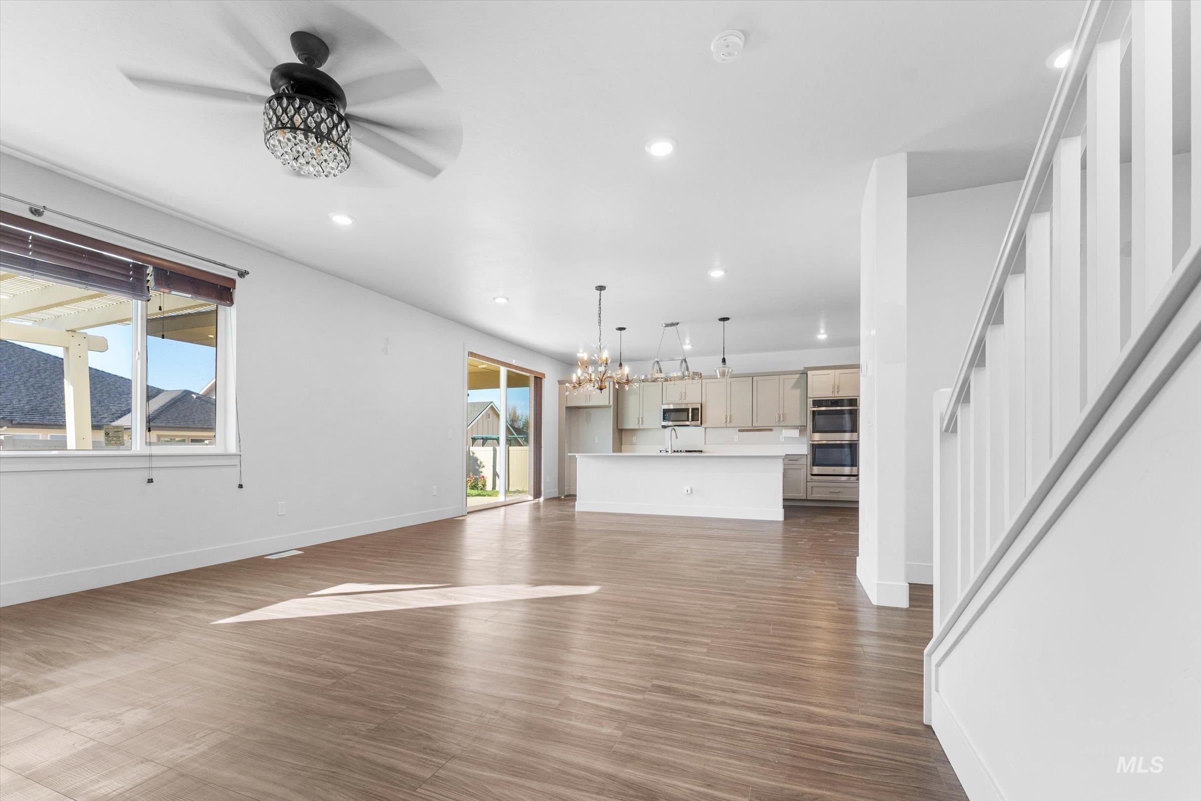 Unfurnished living room featuring a chandelier, recessed lighting, dark wood-style flooring, a ceiling fan, and stairway