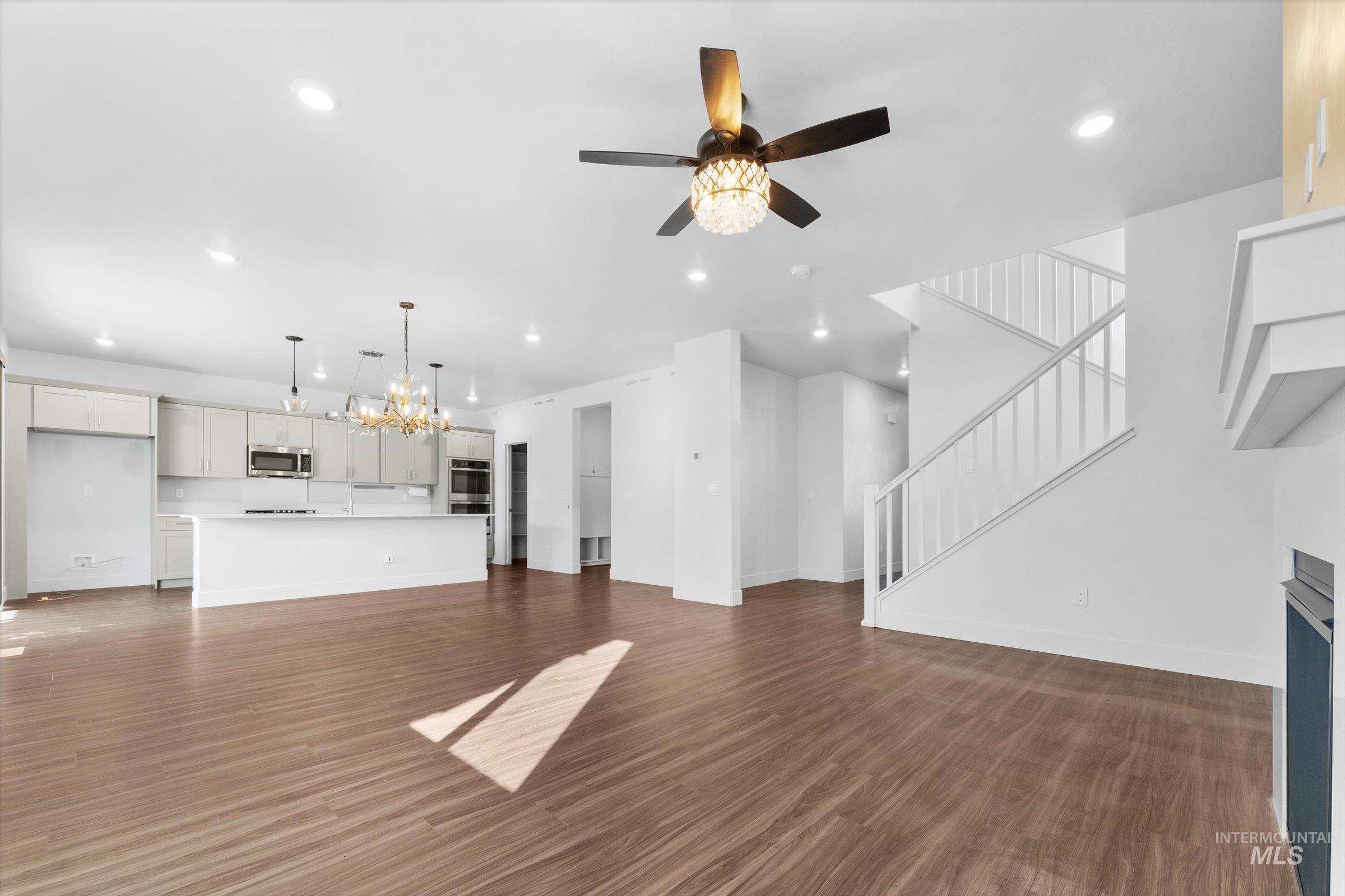 Unfurnished living room with a chandelier, dark wood finished floors, a ceiling fan, stairway, and recessed lighting