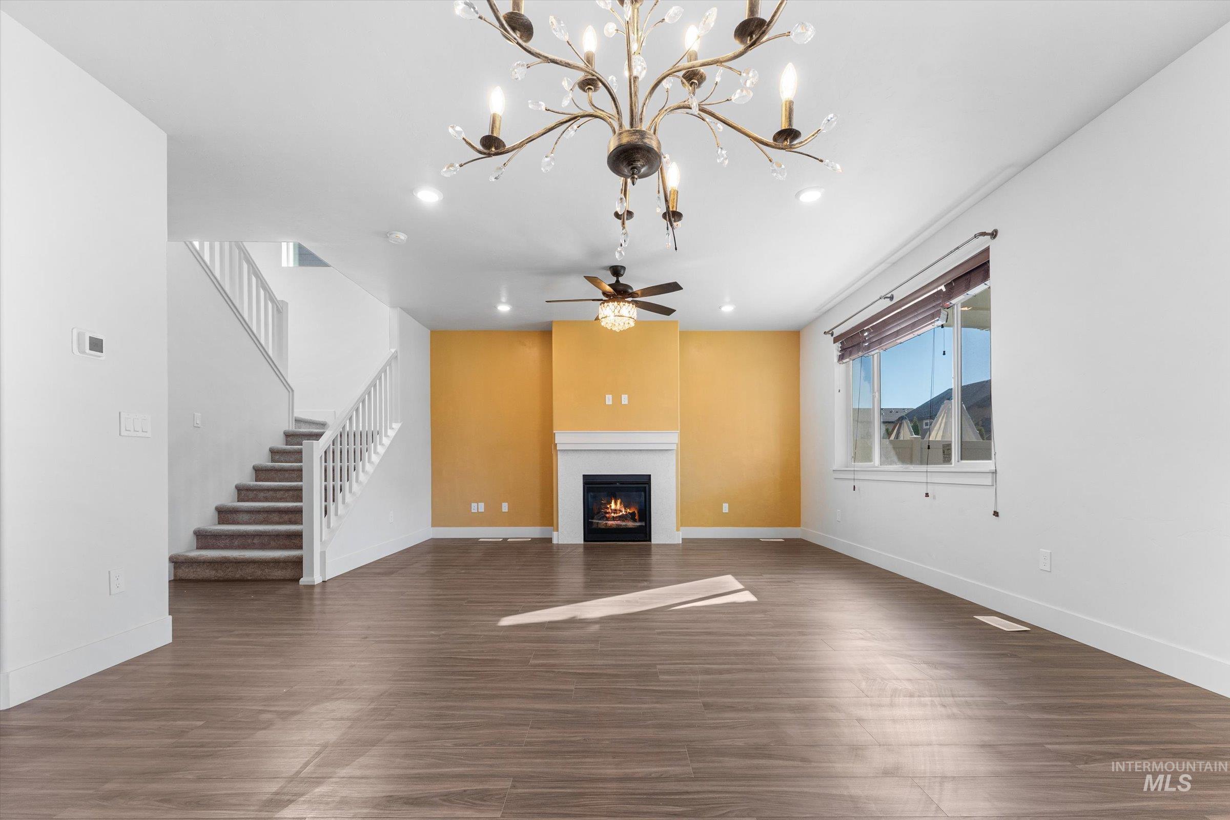 Unfurnished living room featuring a glass covered fireplace, dark wood-style floors, stairway, recessed lighting, and ceiling fan