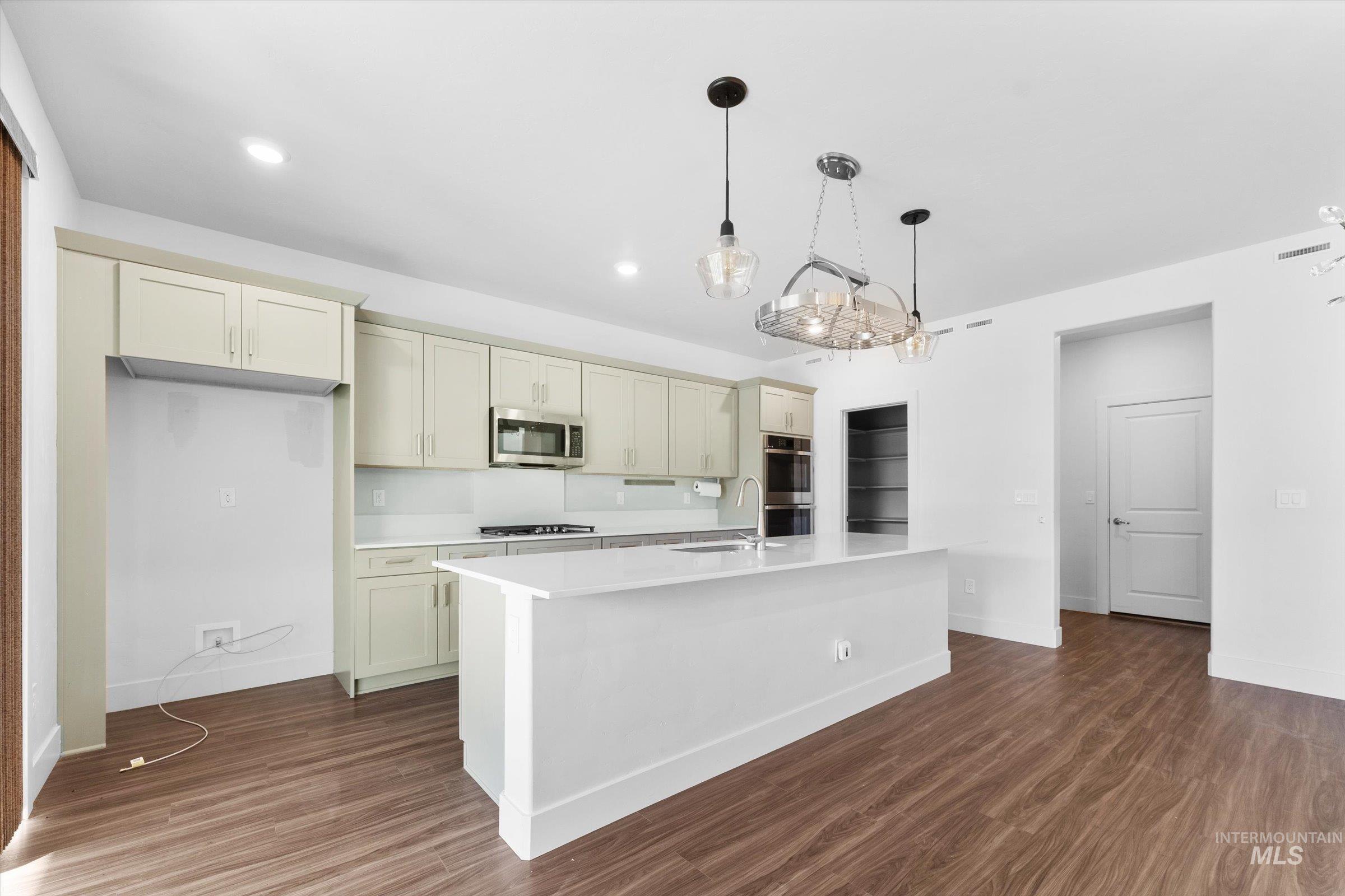 Kitchen with decorative light fixtures, dark wood-style floors, cream cabinetry, appliances with stainless steel finishes, and recessed lighting