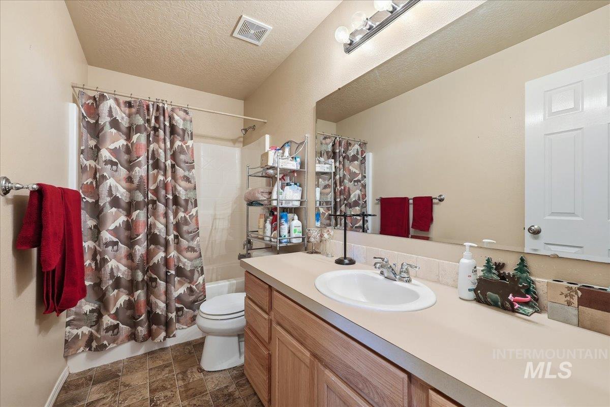 Bathroom featuring shower / tub combo, a textured ceiling, vanity, and stone finish flooring