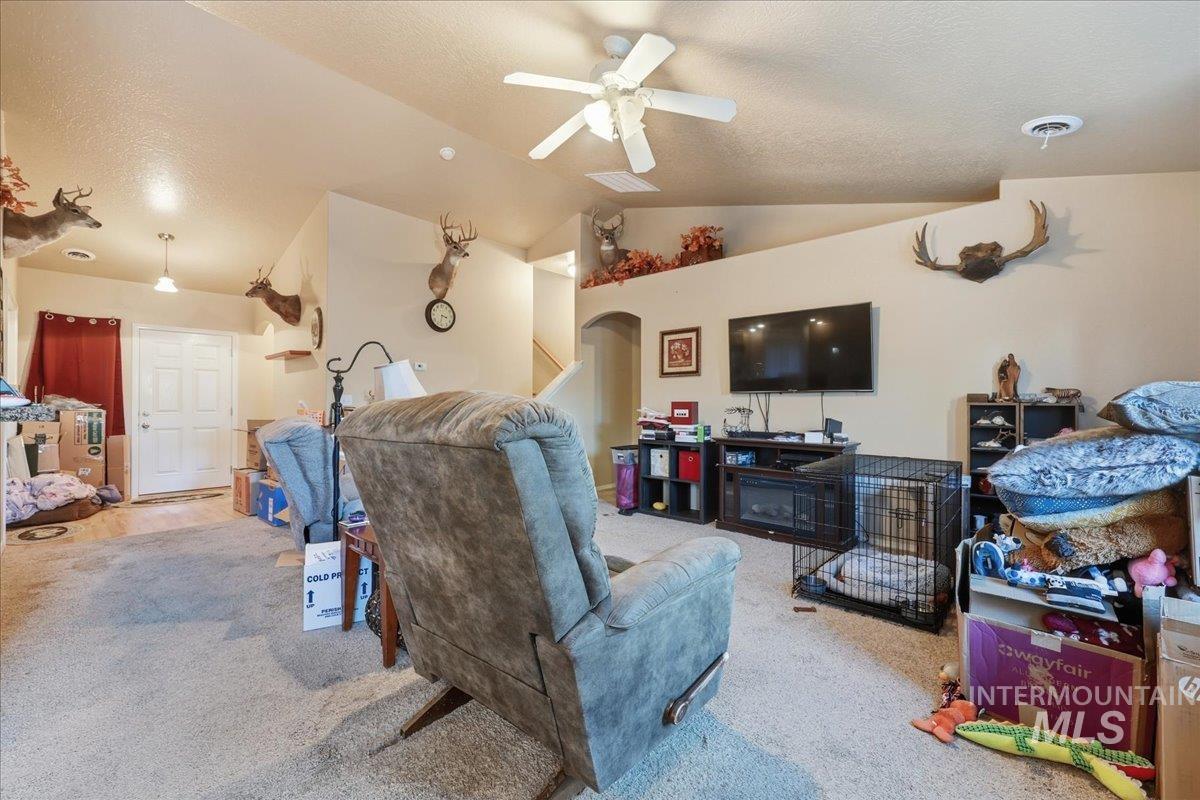 Living room with a textured ceiling, vaulted ceiling, light carpet, and ceiling fan