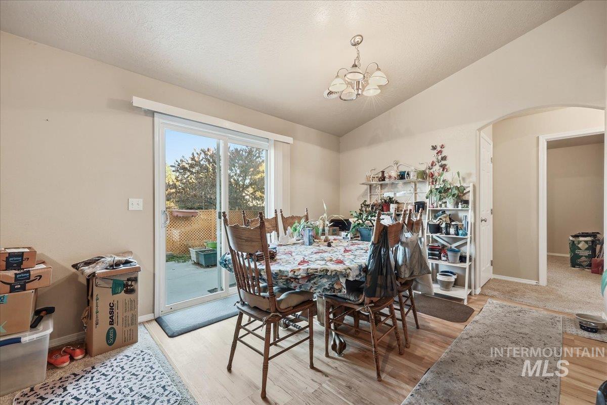 Dining area featuring lofted ceiling, light wood-style flooring, a chandelier, and a textured ceiling