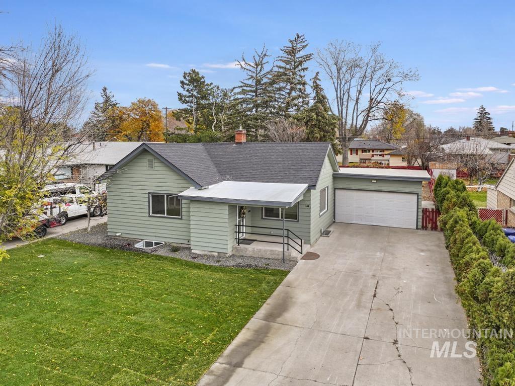 View of front of house featuring driveway, a front yard, a chimney, roof with shingles, and an attached garage