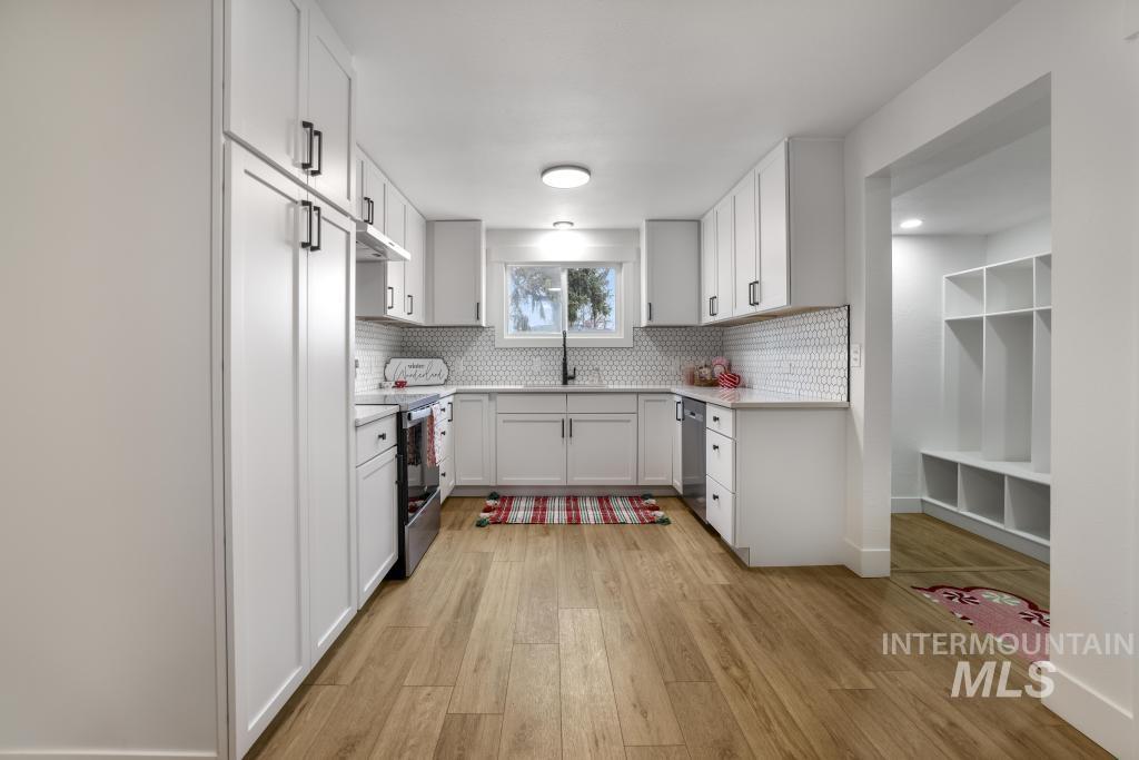 Kitchen featuring light wood-type flooring, tasteful backsplash, stainless steel appliances, white cabinets, and under cabinet range hood