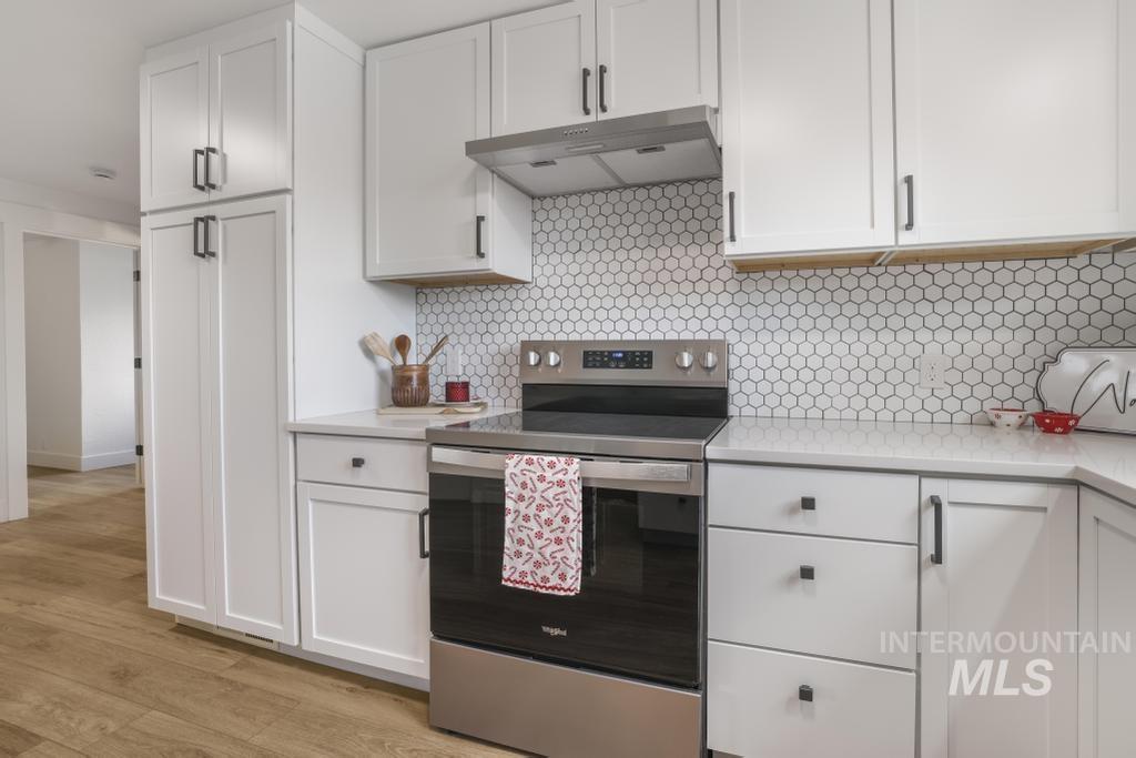 Kitchen with electric range, white cabinets, decorative backsplash, under cabinet range hood, and light stone countertops