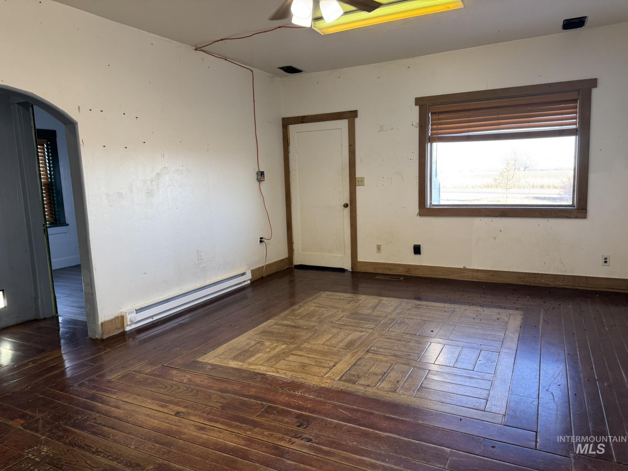 Spare room featuring a baseboard heating unit, arched walkways, dark wood finished floors, and a ceiling fan