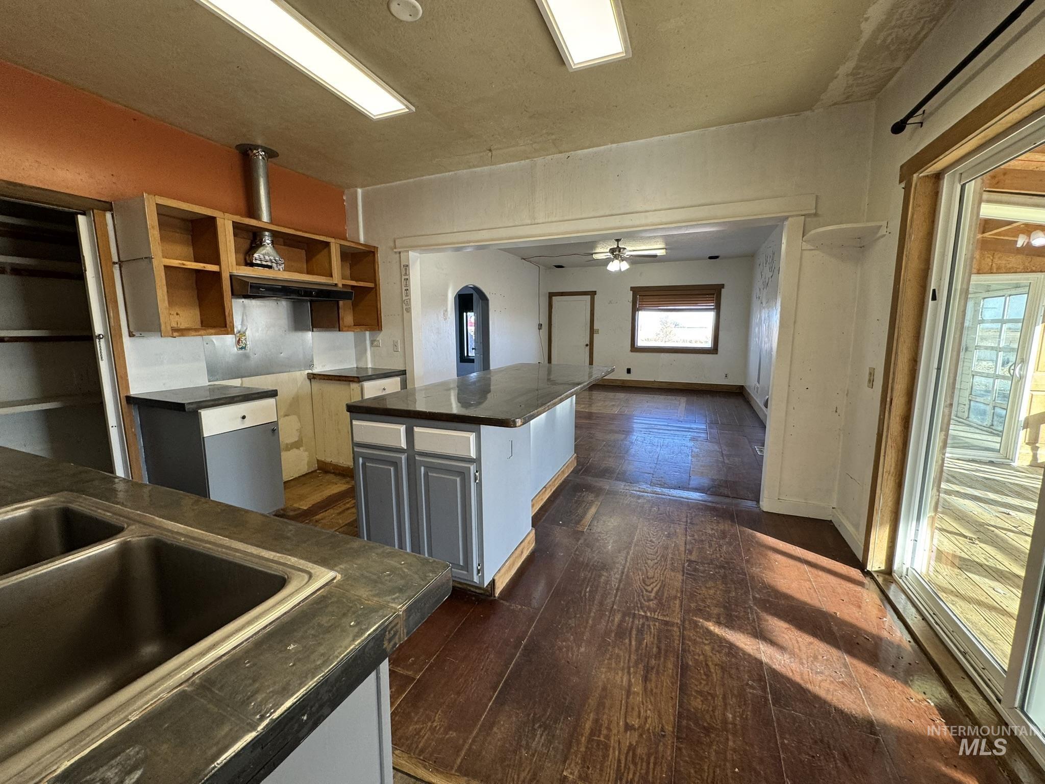 Kitchen with dark wood finished floors, dark countertops, ceiling fan, a center island, and arched walkways