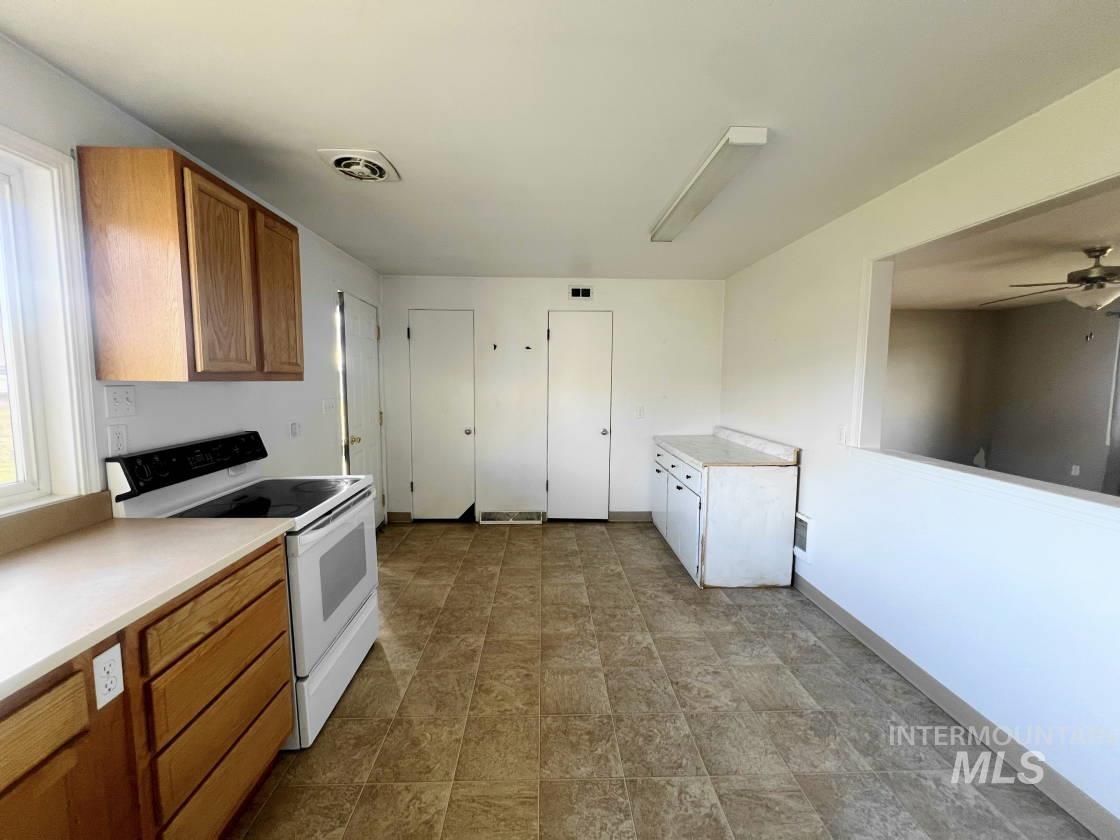 Kitchen with white range with electric stovetop, light countertops, brown cabinetry, a ceiling fan, and stone finish flooring