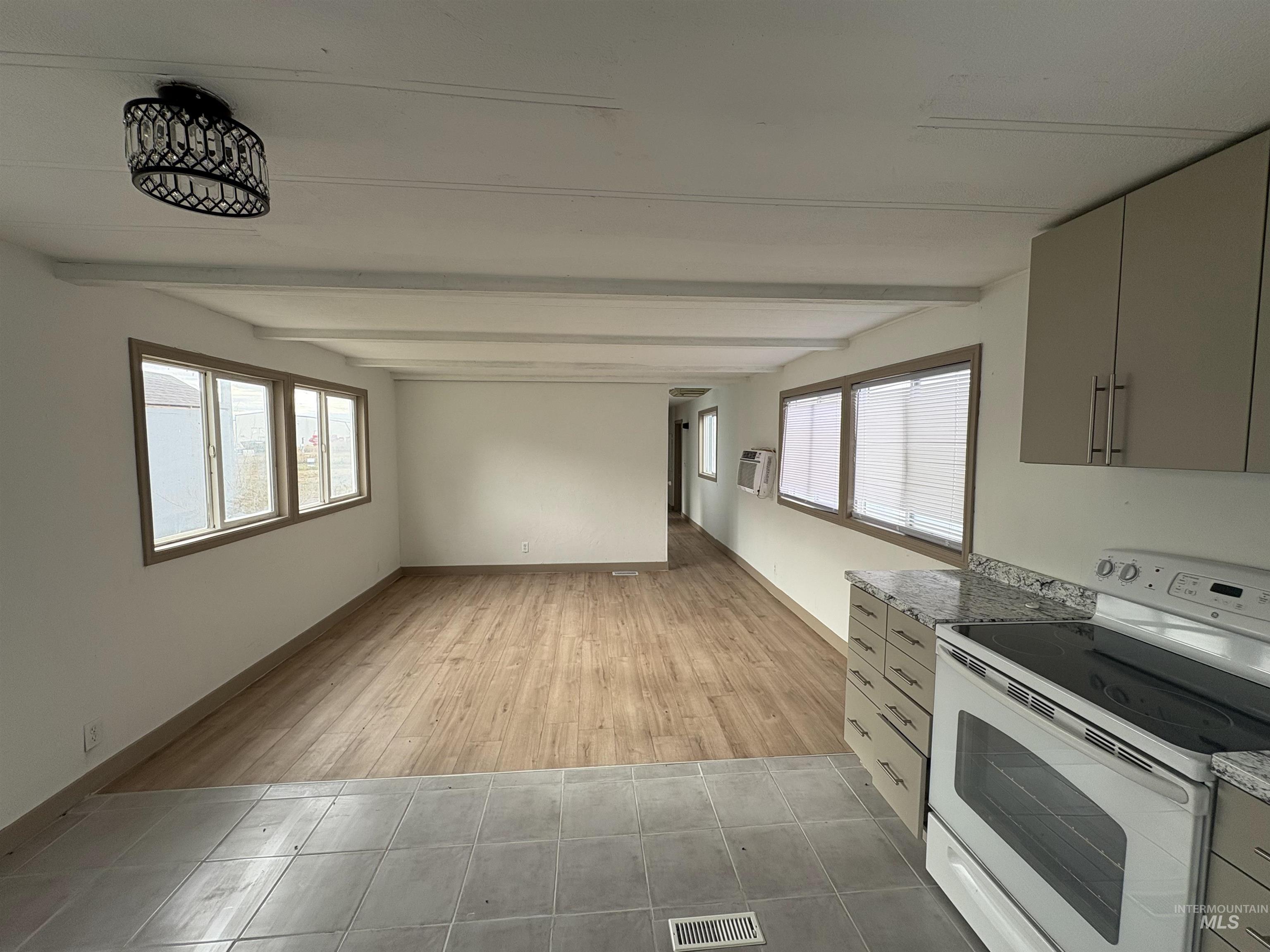 Kitchen with white range with electric cooktop, beamed ceiling, gray cabinetry, light tile patterned flooring, and dark stone countertops