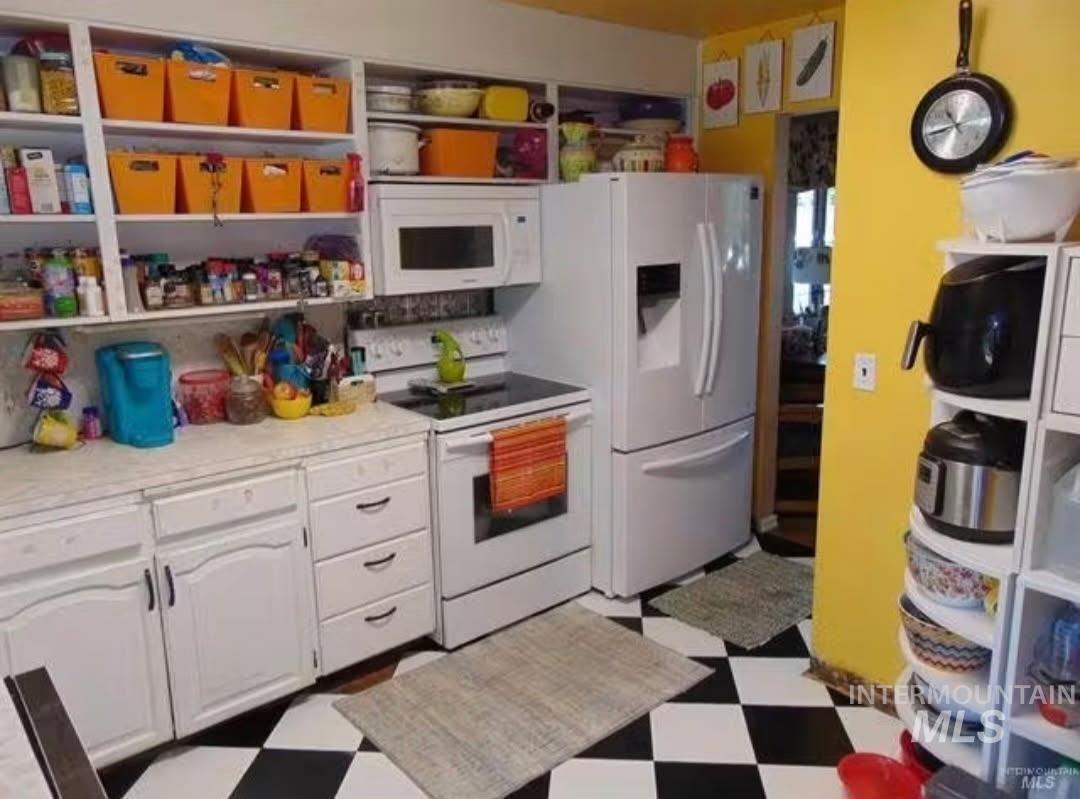 Kitchen with dark floors, white appliances, white cabinets, and light countertops