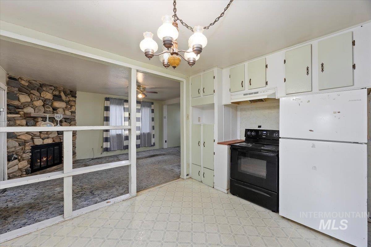 Kitchen featuring freestanding refrigerator, black electric range oven, a ceiling fan, a fireplace, and a chandelier