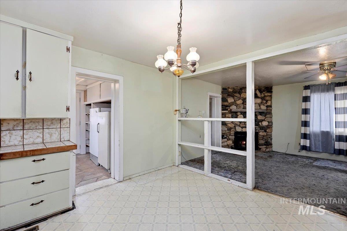 Unfurnished dining area featuring a chandelier, a stone fireplace, a ceiling fan, and light floors