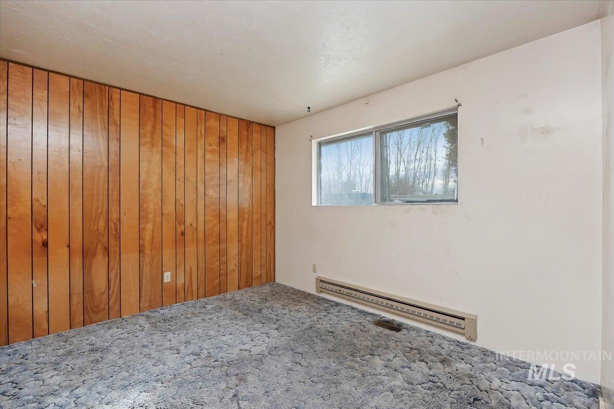 Carpeted spare room featuring wood walls and a baseboard radiator