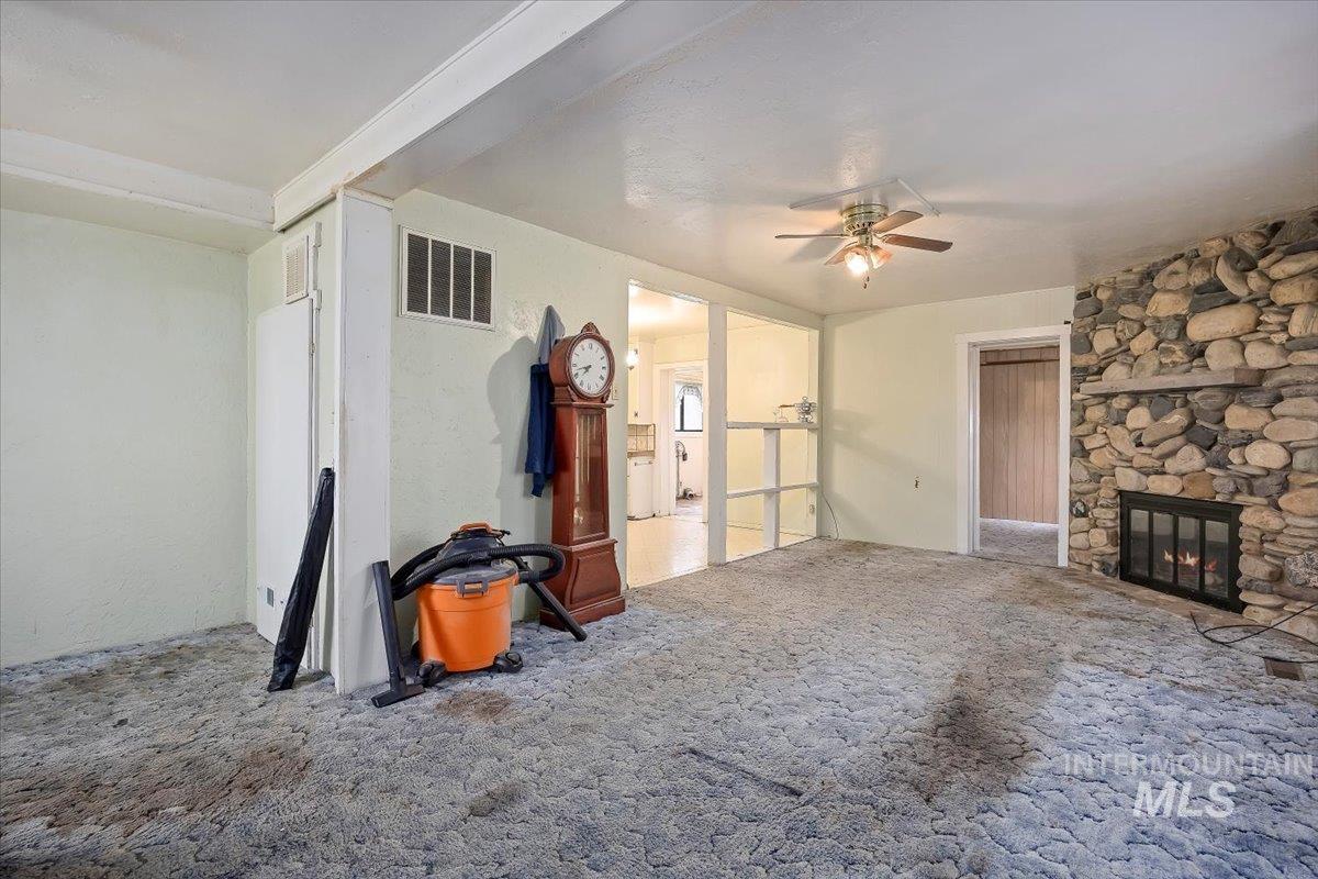 Unfurnished living room featuring carpet flooring, a stone fireplace, and ceiling fan