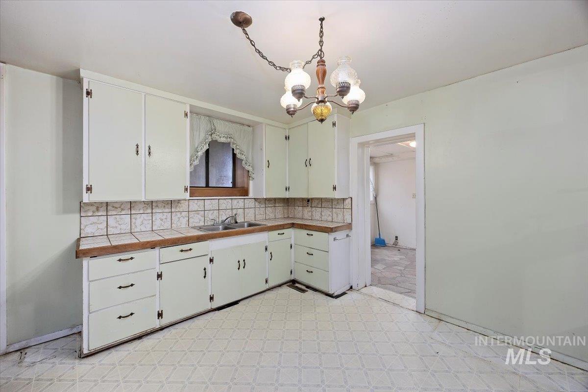 Kitchen featuring backsplash, decorative light fixtures, a chandelier, light floors, and white cabinetry