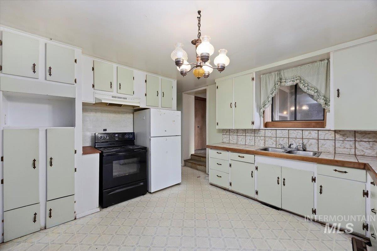Kitchen featuring tasteful backsplash, black range with electric cooktop, a chandelier, freestanding refrigerator, and light flooring