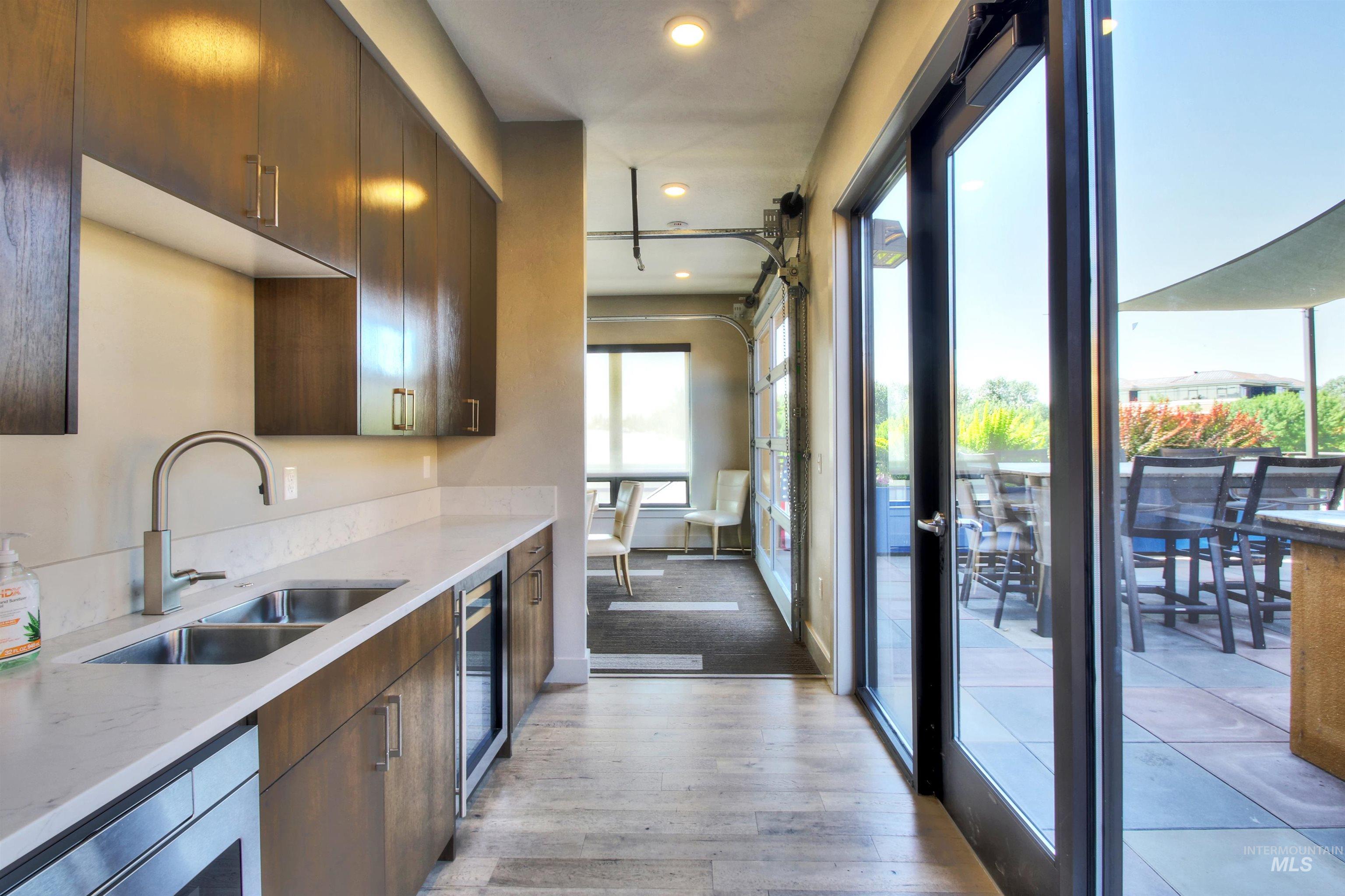 Kitchen with light stone countertops, light wood-type flooring, recessed lighting, wine cooler, and dark brown cabinetry