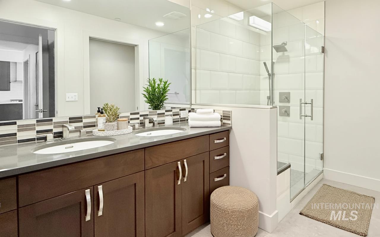 Full bath with double vanity, a shower stall, decorative backsplash, and recessed lighting