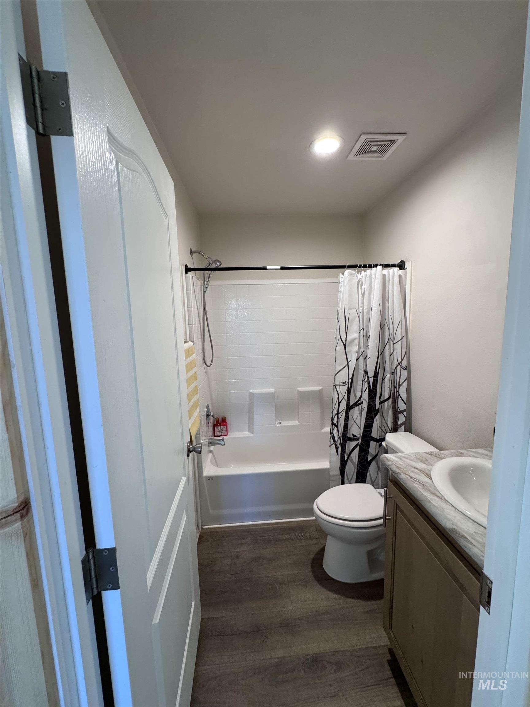 Bathroom featuring dark wood finished floors, vanity, shower / bathtub combination with curtain, and recessed lighting