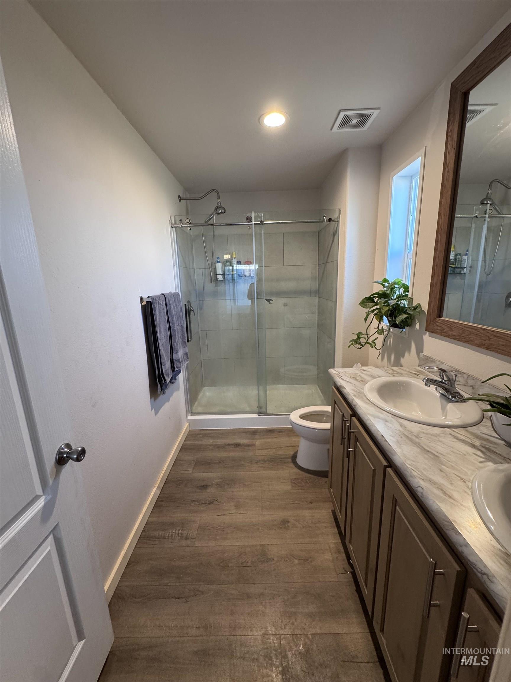 Bathroom featuring dark wood-style floors, double vanity, a shower stall, and recessed lighting