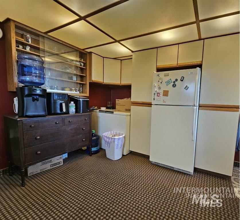 Kitchen featuring freestanding refrigerator, dark colored carpet, and open shelves