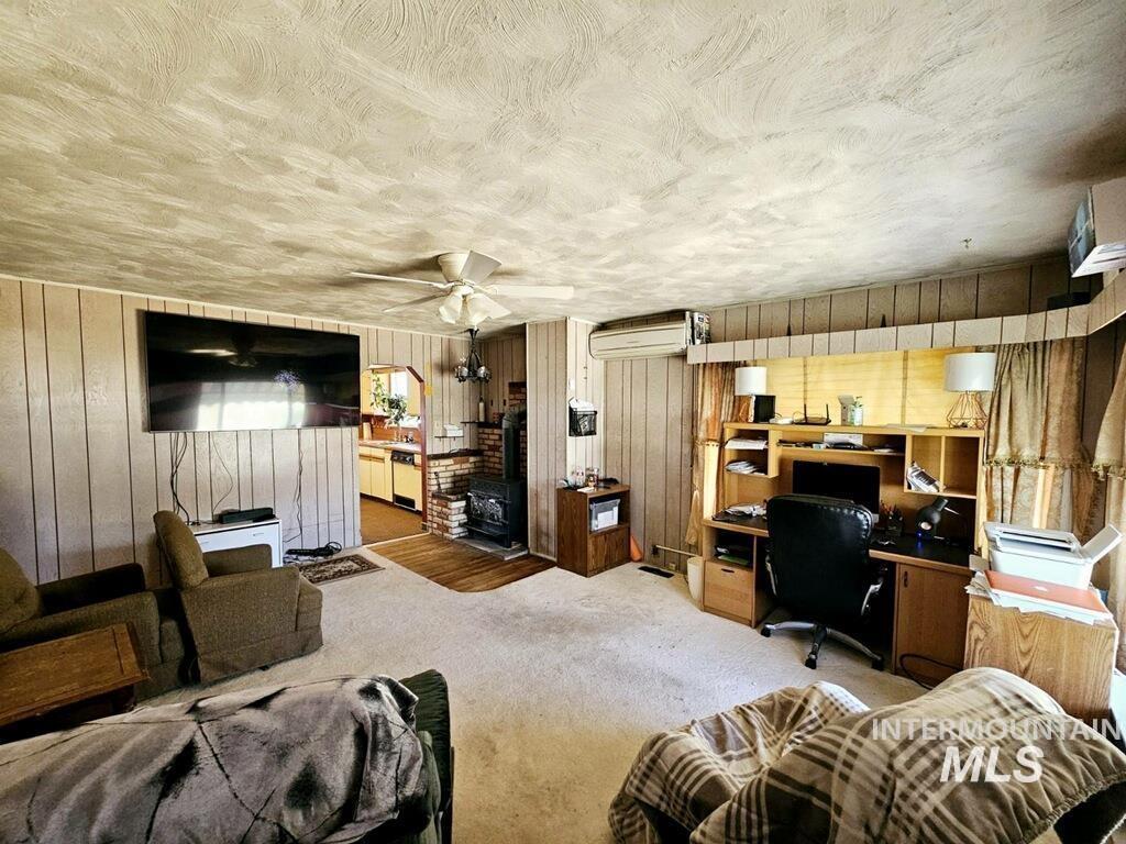 Home office with carpet, wooden walls, ceiling fan, and a textured ceiling
