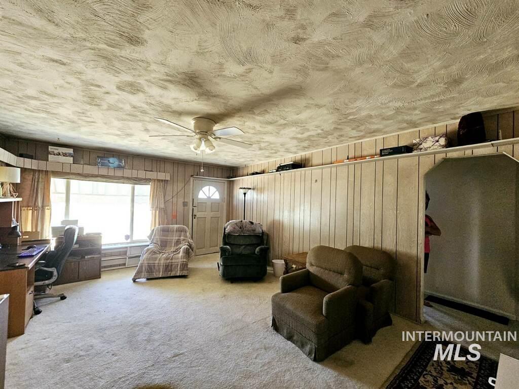 Living area featuring an office area, carpet, wooden walls, a textured ceiling, and a ceiling fan