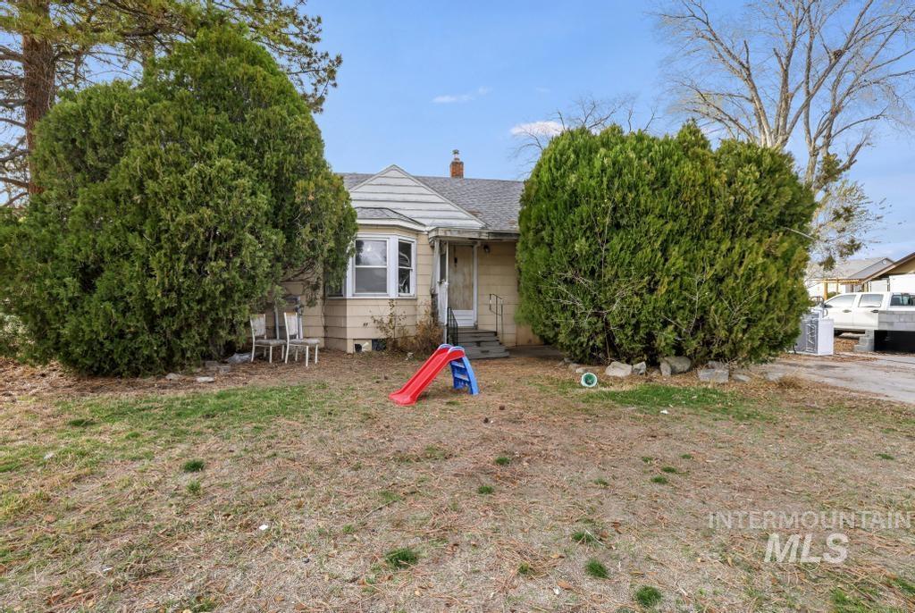 View of property hidden behind natural elements featuring a chimney and a shingled roof