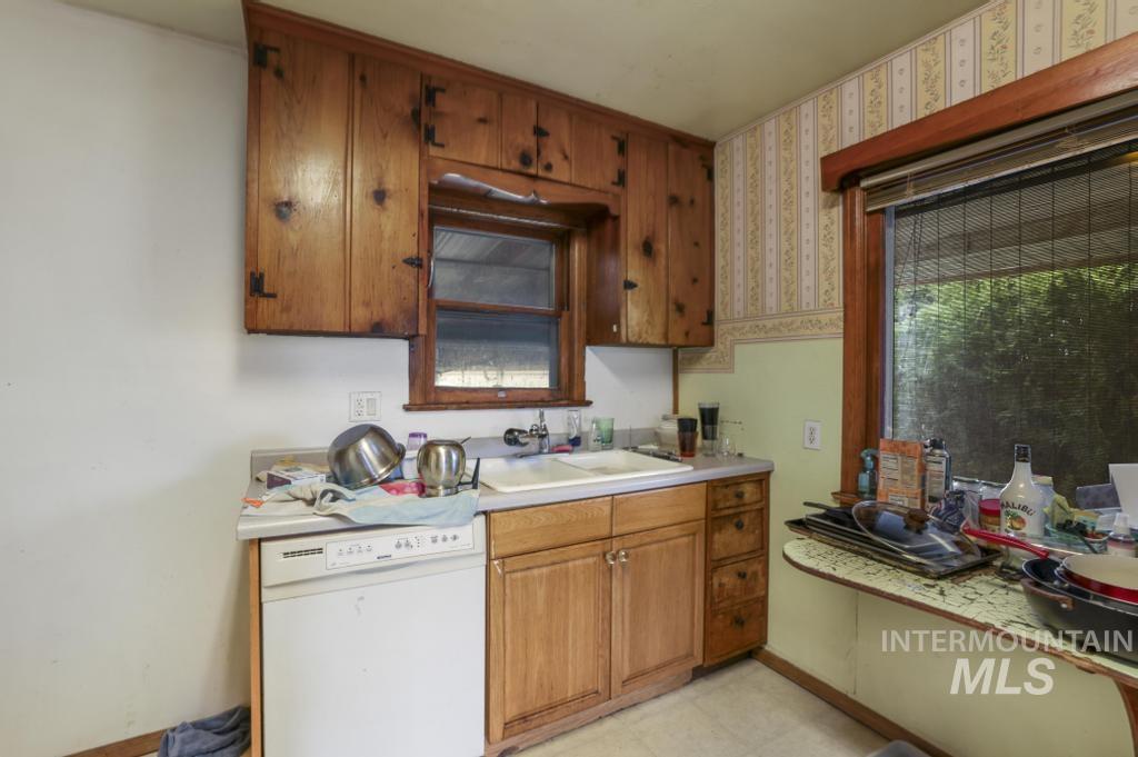 Kitchen with white dishwasher, light countertops, brown cabinetry, wallpapered walls, and light floors