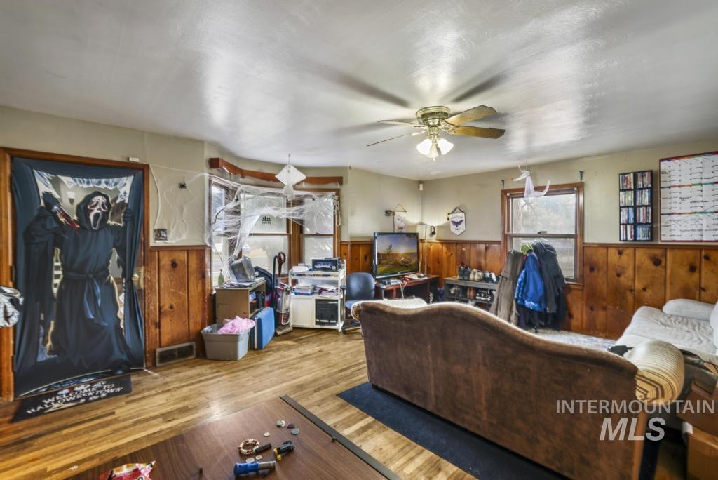 Living room featuring wood walls, wood finished floors, wainscoting, and ceiling fan