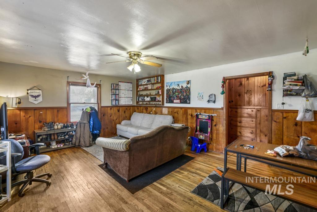 Living area with wood-type flooring, ceiling fan, a wainscoted wall, and wood walls